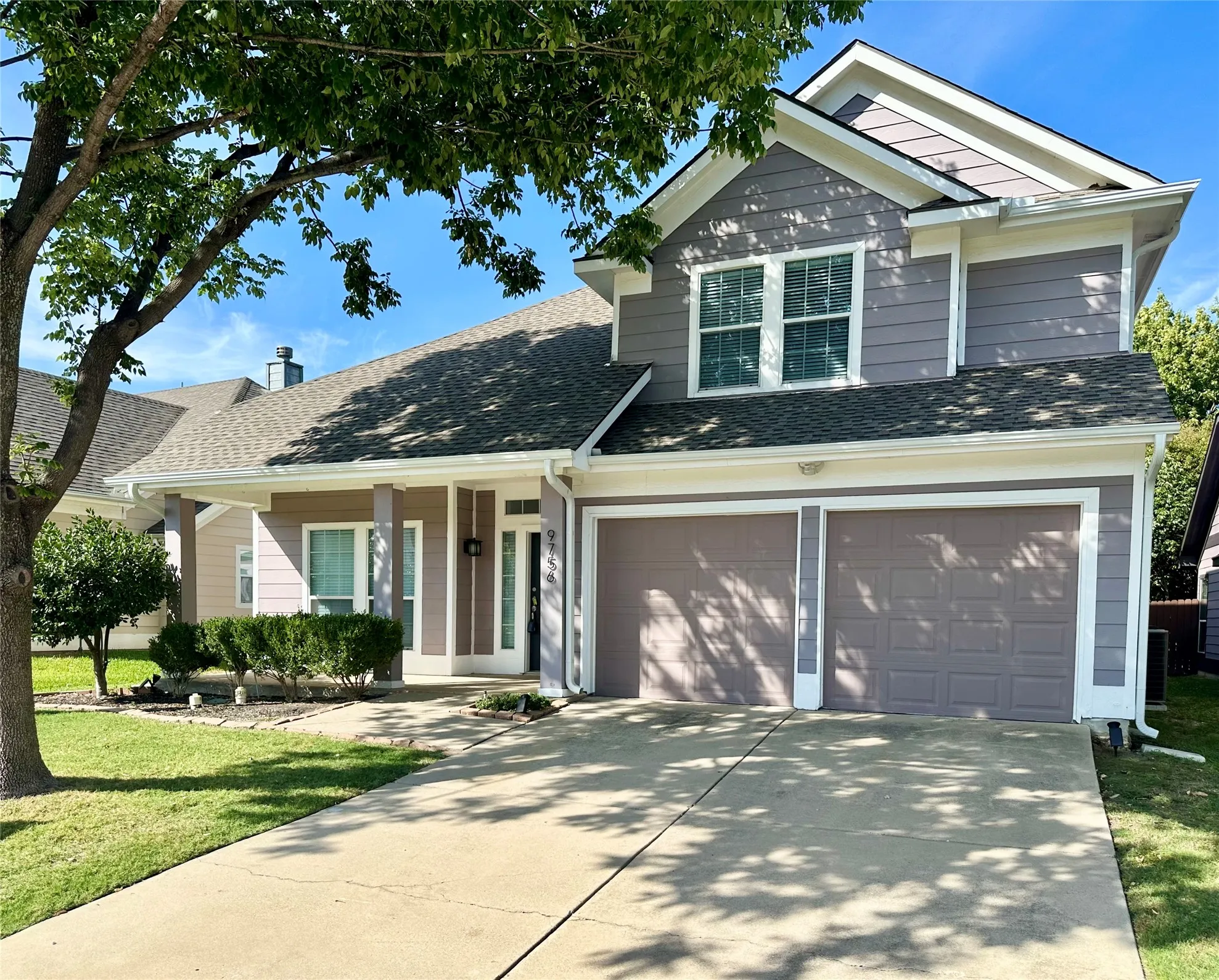 Exterior facade featuring horizontal lap siding, a pitched shingle roof, a two-car garage, and a covered front porch with square columns