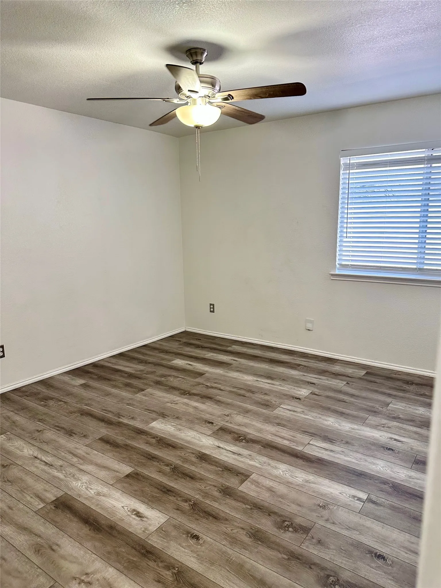 Wood-finish flooring, neutral walls, brushed metal ceiling fan with integrated light fixture, and horizontal window blinds