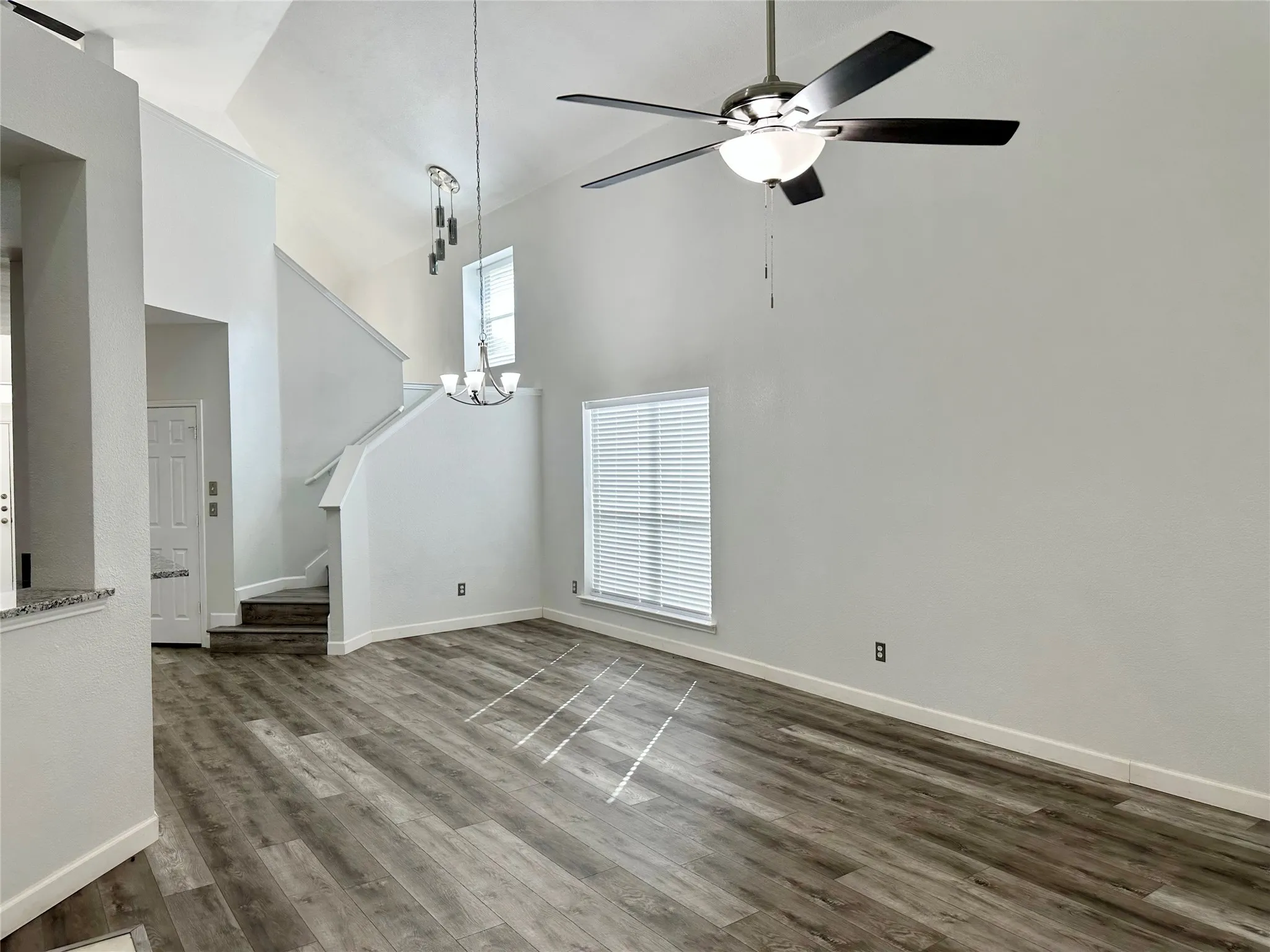 Vaulted ceiling featuring a multi-blade ceiling fan with integrated lighting, wood-finish flooring, and dual-level hanging pendant lighting