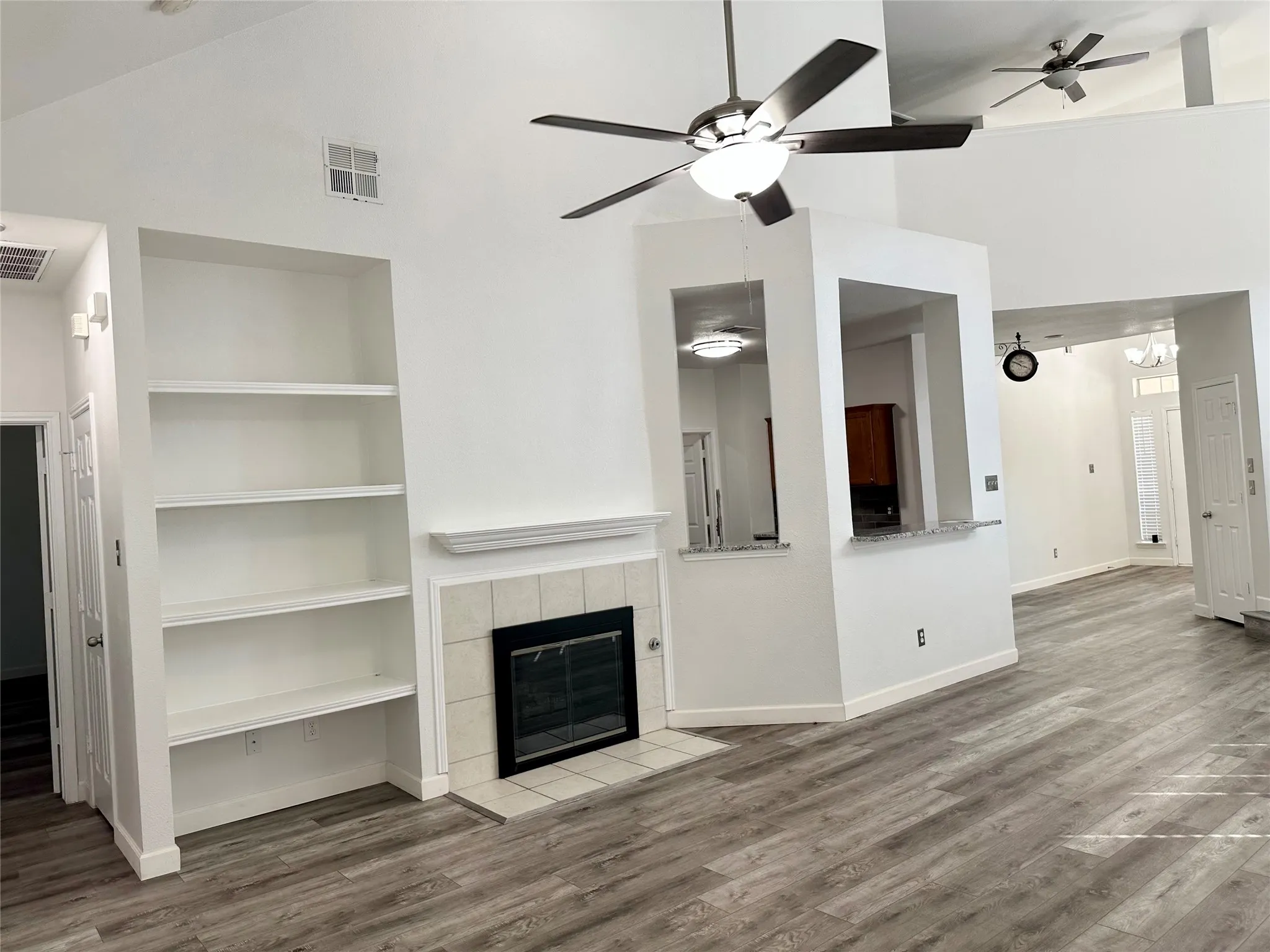 Vaulted ceilings with recessed lighting, tile-surround fireplace, built-in shelving, hard-surface flooring, and kitchen pass-through counter