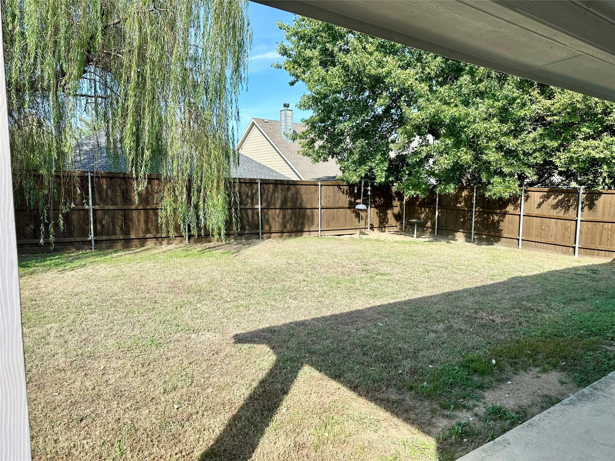 Private backyard featuring a concrete patio, perimeter wood privacy fencing, a grass lawn, and mature canopy trees