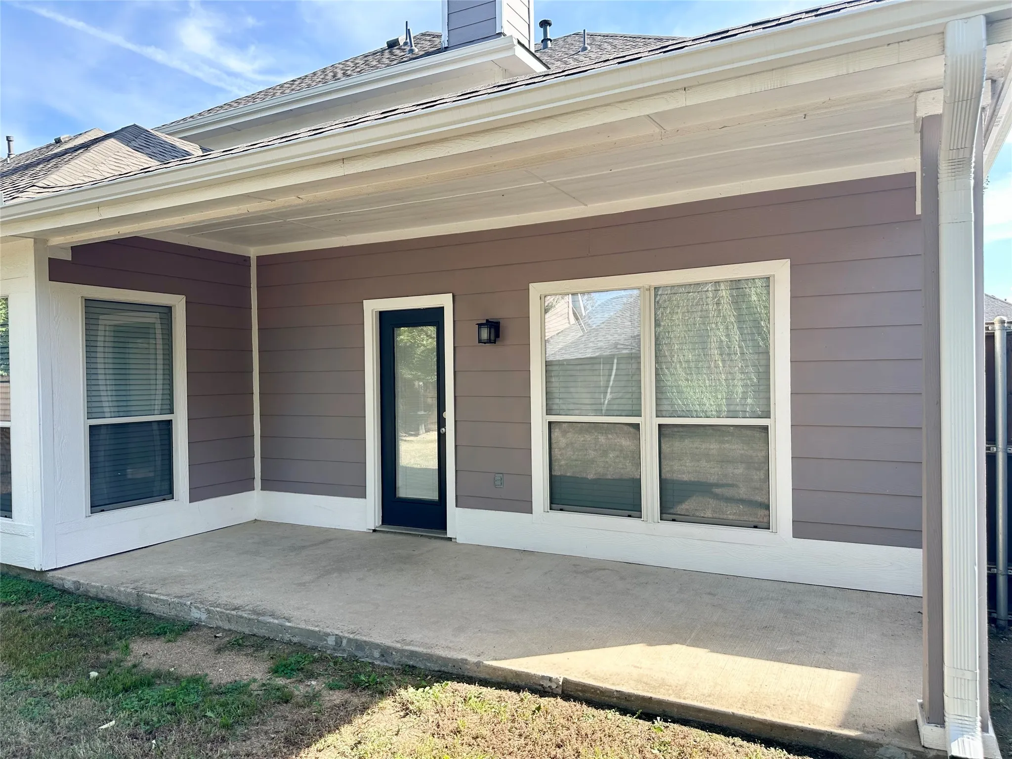 Covered concrete patio featuring horizontal siding, exterior wall-mounted lighting, and a glass-paneled door