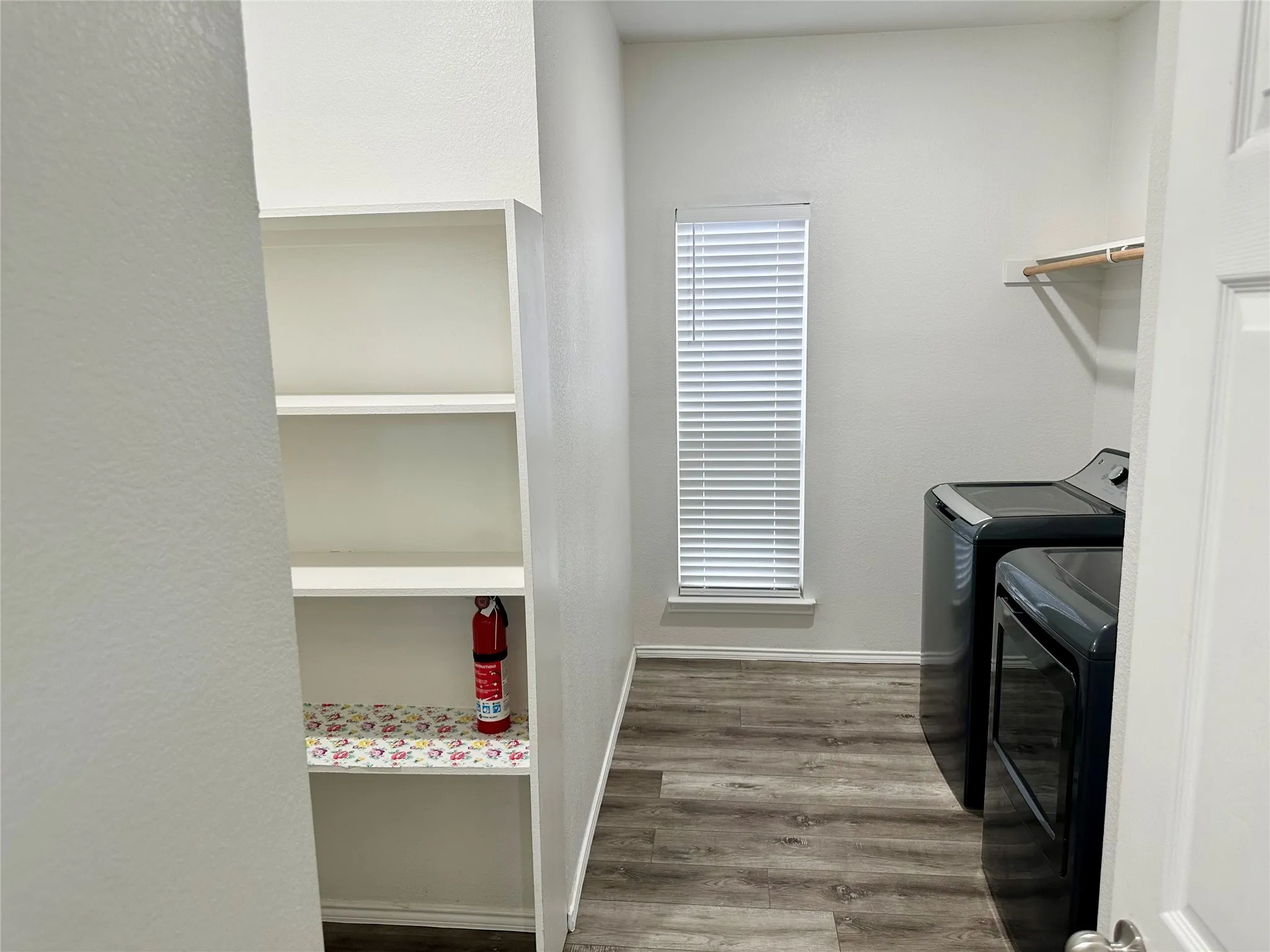 Utility space featuring wood-finish flooring, built-in shelving, a window with horizontal blinds, and a mounted hanging rod