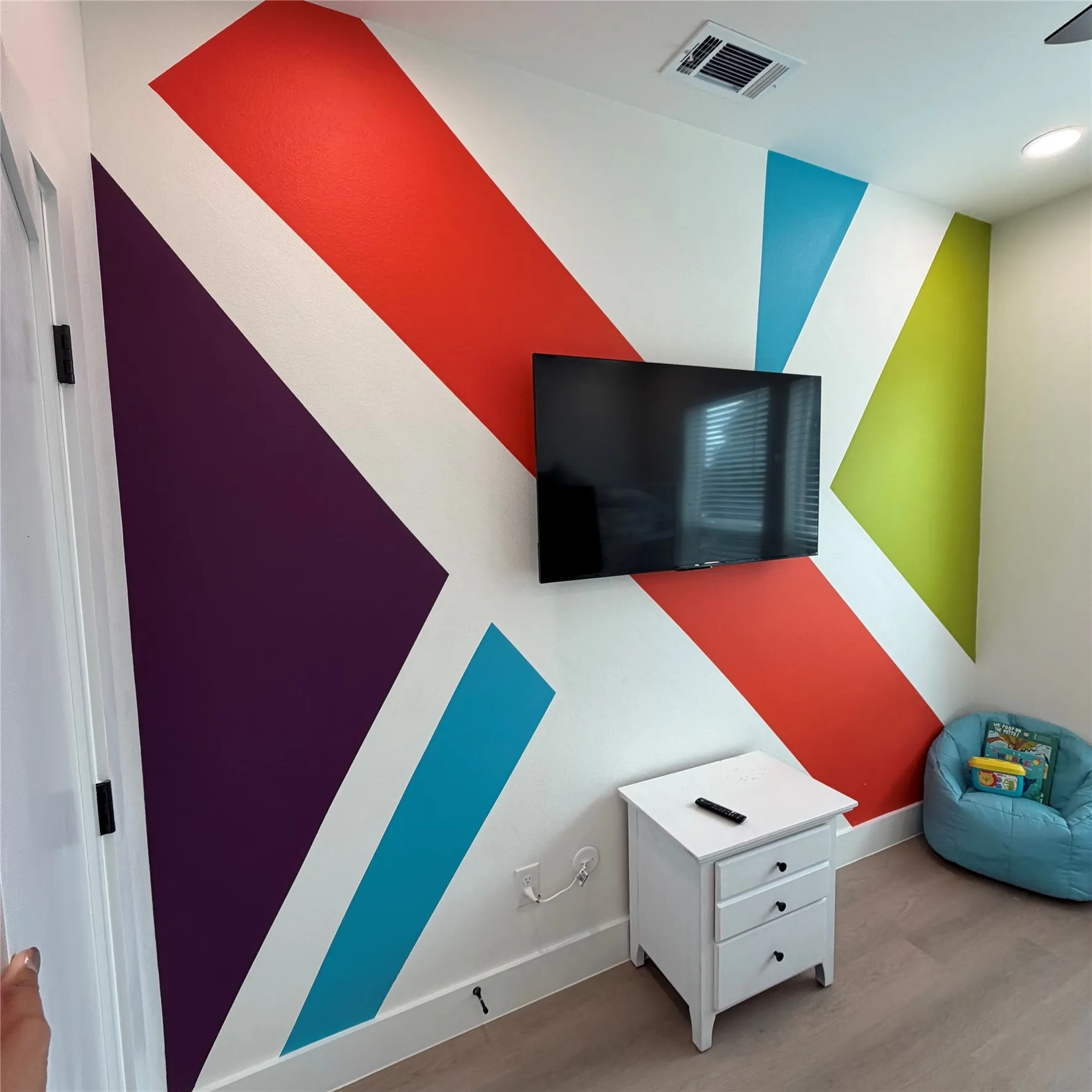 Accent wall featuring bold geometric painted patterns, neutral wood-finish flooring, and recessed ceiling lighting