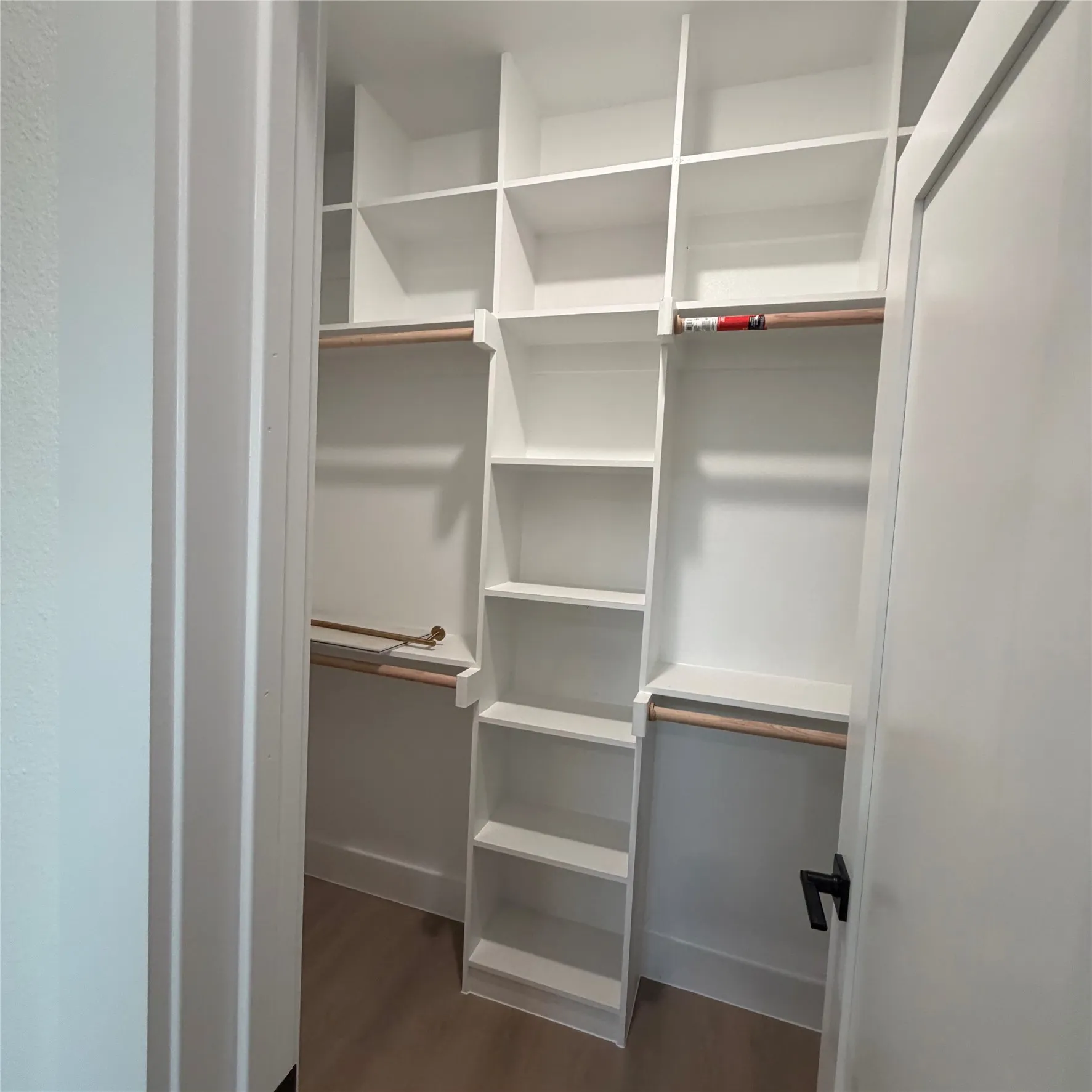 Custom closet featuring white built-in shelving, wood-finish hanging rods, and wood-finish flooring