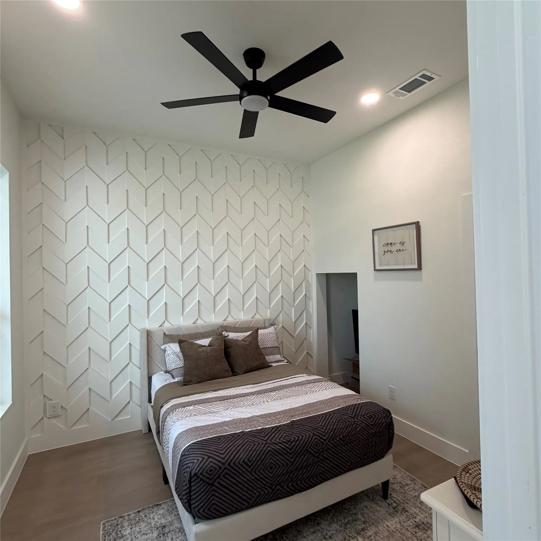 Geometric custom wood wall detailing, wood-finish flooring, and a matte black ceiling fan