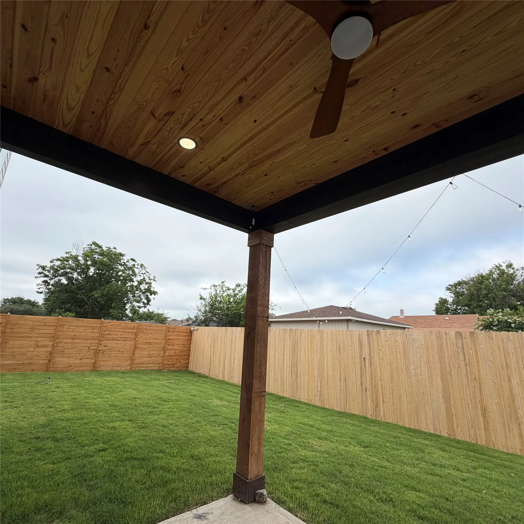 Covered patio featuring a wood-plank ceiling, recessed lighting, and a ceiling fan, opening to a 8ft fenced backyard with a grass lawn