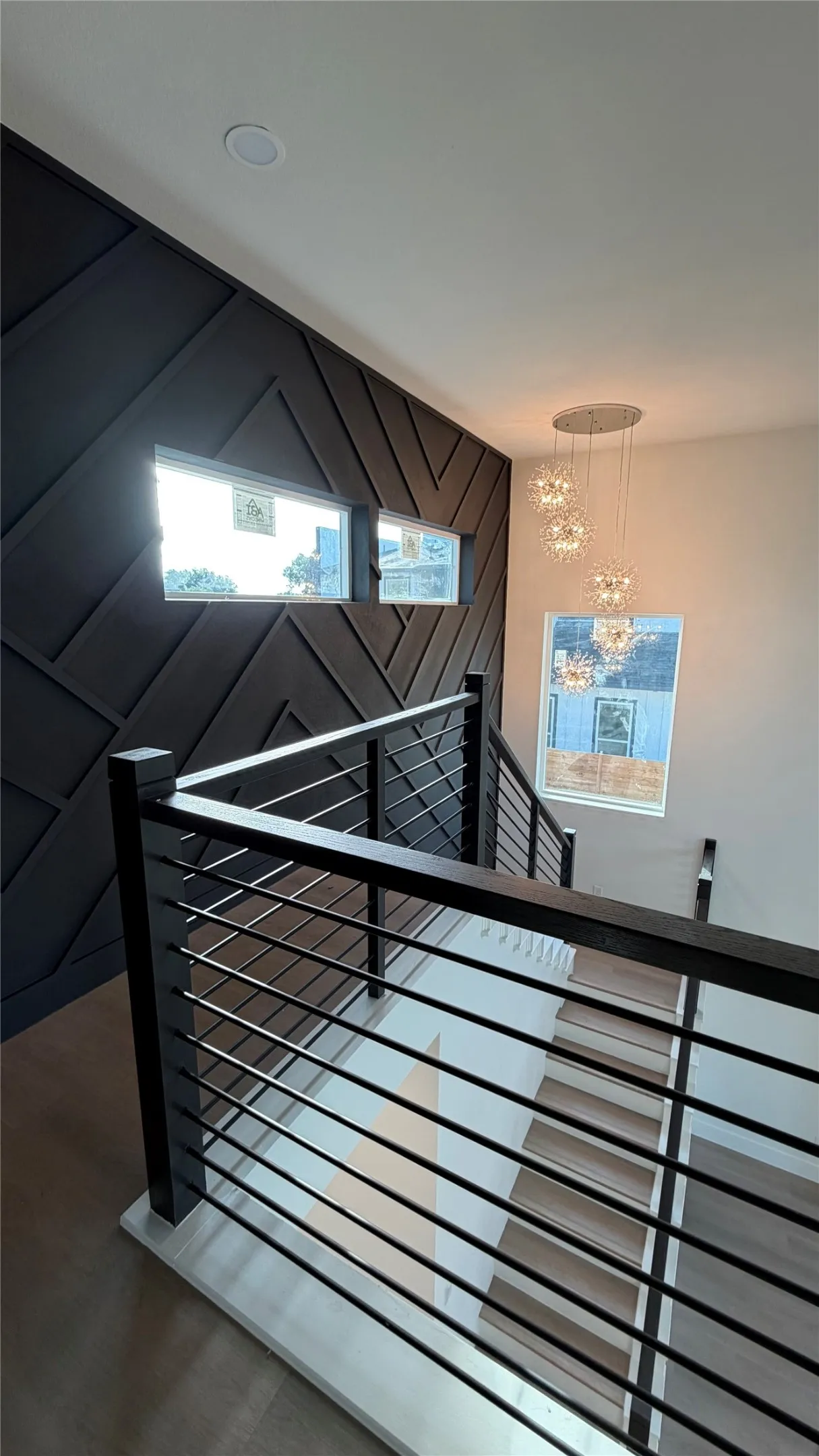 Staircase featuring a geometric dark-toned accent wall, cable railing system, wood-finish treads, and multi-tier pendant lighting