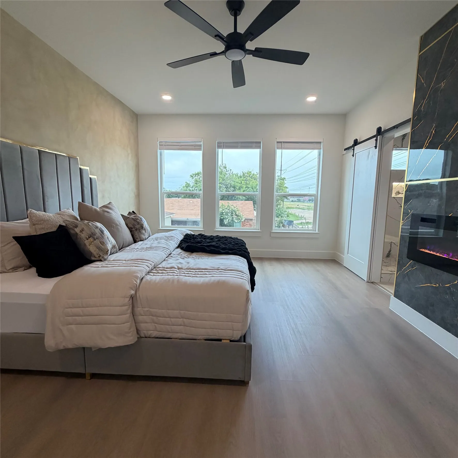 Floor-to-ceiling accent wall with integrated fireplace, wood-finish flooring, matte black ceiling fan, recessed lighting, and sliding barn door
