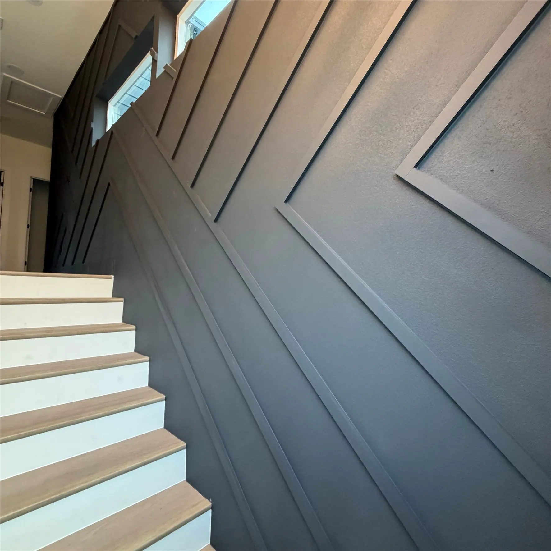 Staircase featuring wood-finish treads, matte dark-toned geometric wall paneling, and integrated recessed lighting