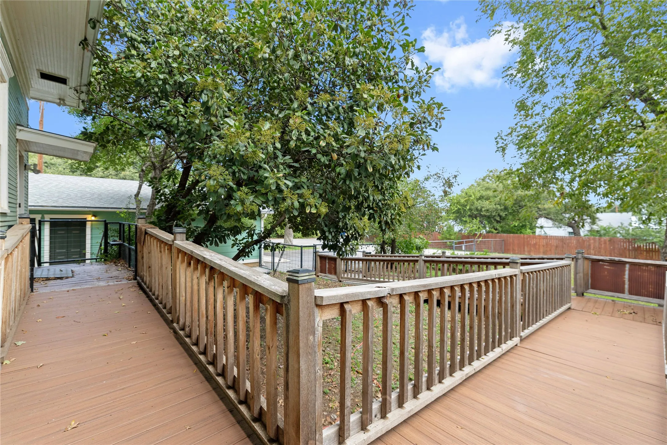 Multi-level wooden deck featuring vertical balusters, post caps, and mature tree canopy