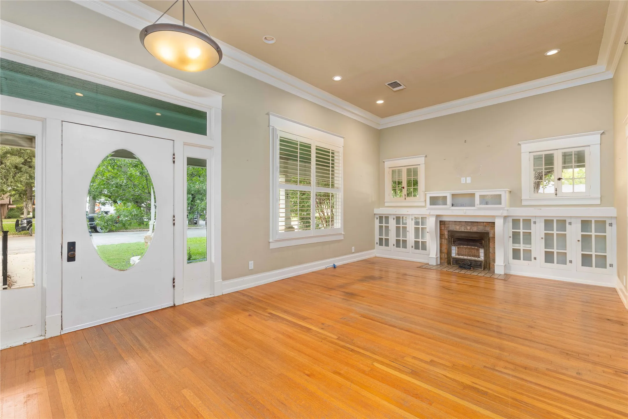 Wood-finish flooring, fireplace with white mantle and built-in glass-front cabinetry, crown molding, and recessed lighting