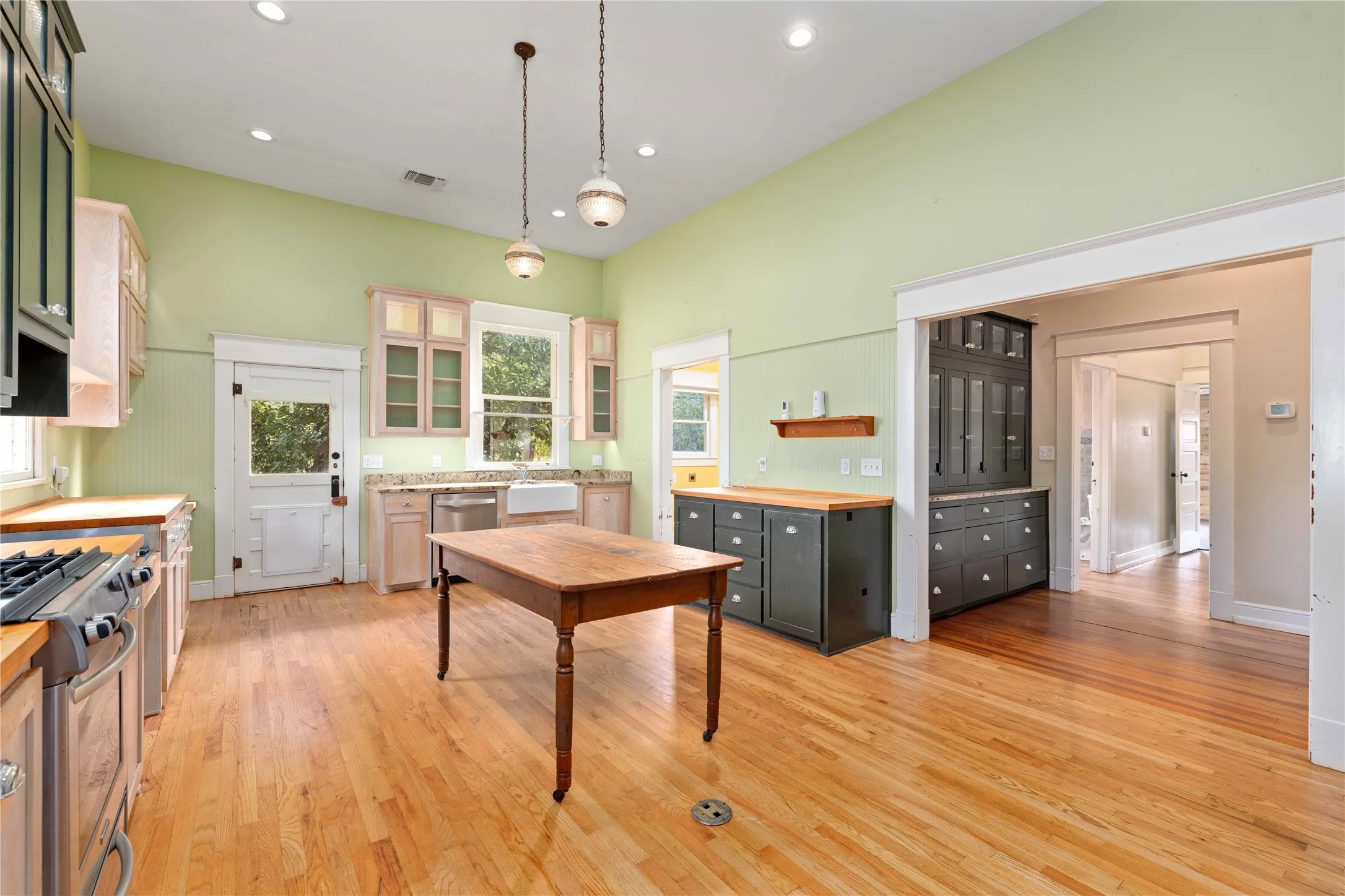 Kitchen featuring high ceilings, wood-finish flooring, stone-surfaced countertops, a farmhouse-style sink, and built-in cabinetry