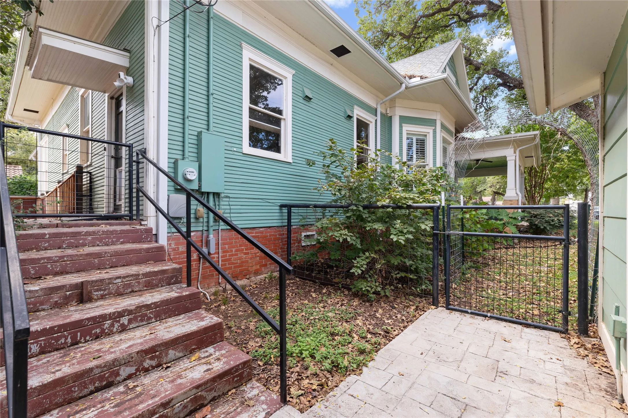 Exterior featuring lap siding, a brick foundation, paver stone walkway, metal fencing, and multi-pane windows