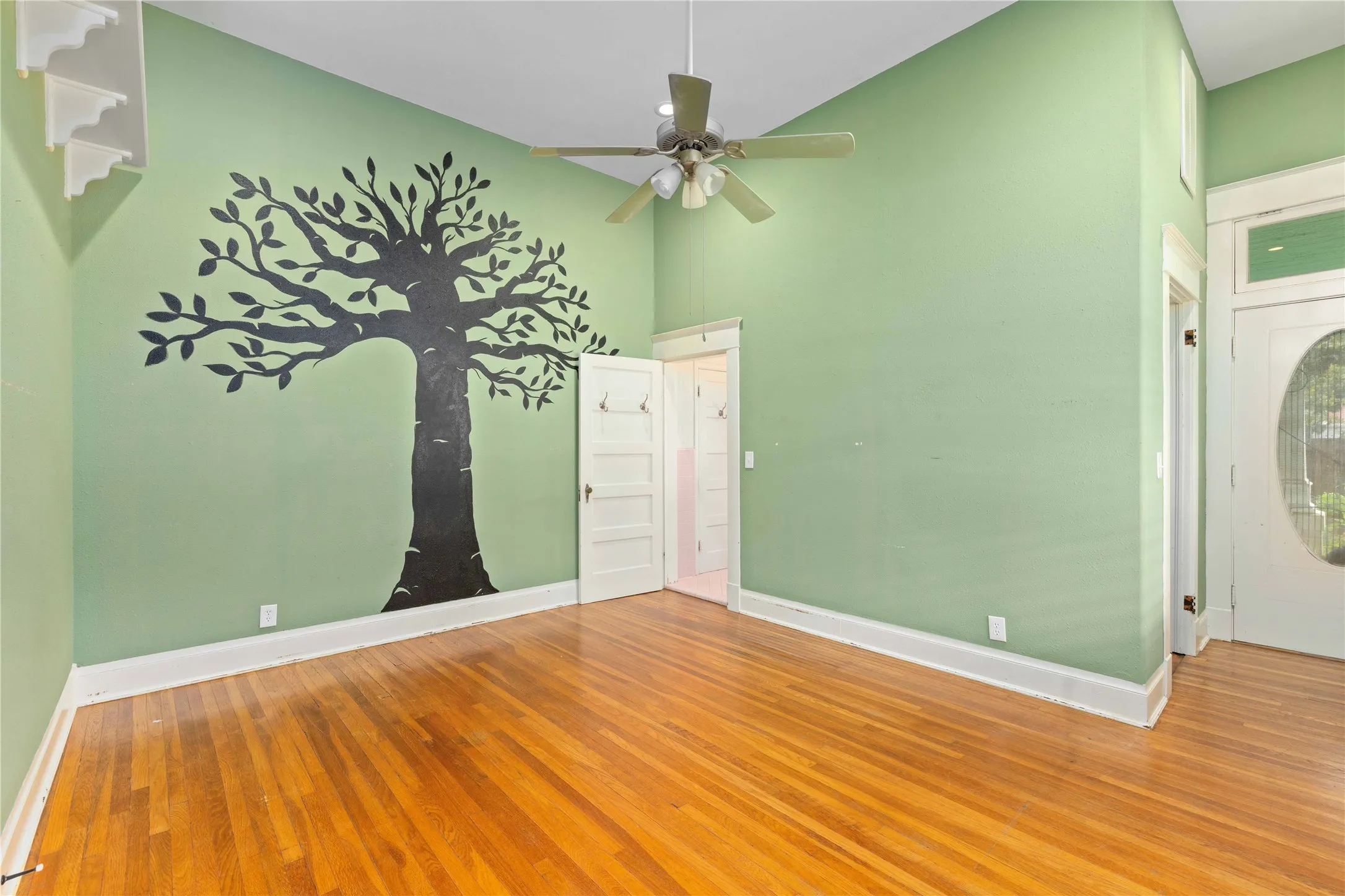High-ceilinged room featuring wood-finish flooring, a multi-blade ceiling fan with integrated lighting, and a solid-core door with a transom window