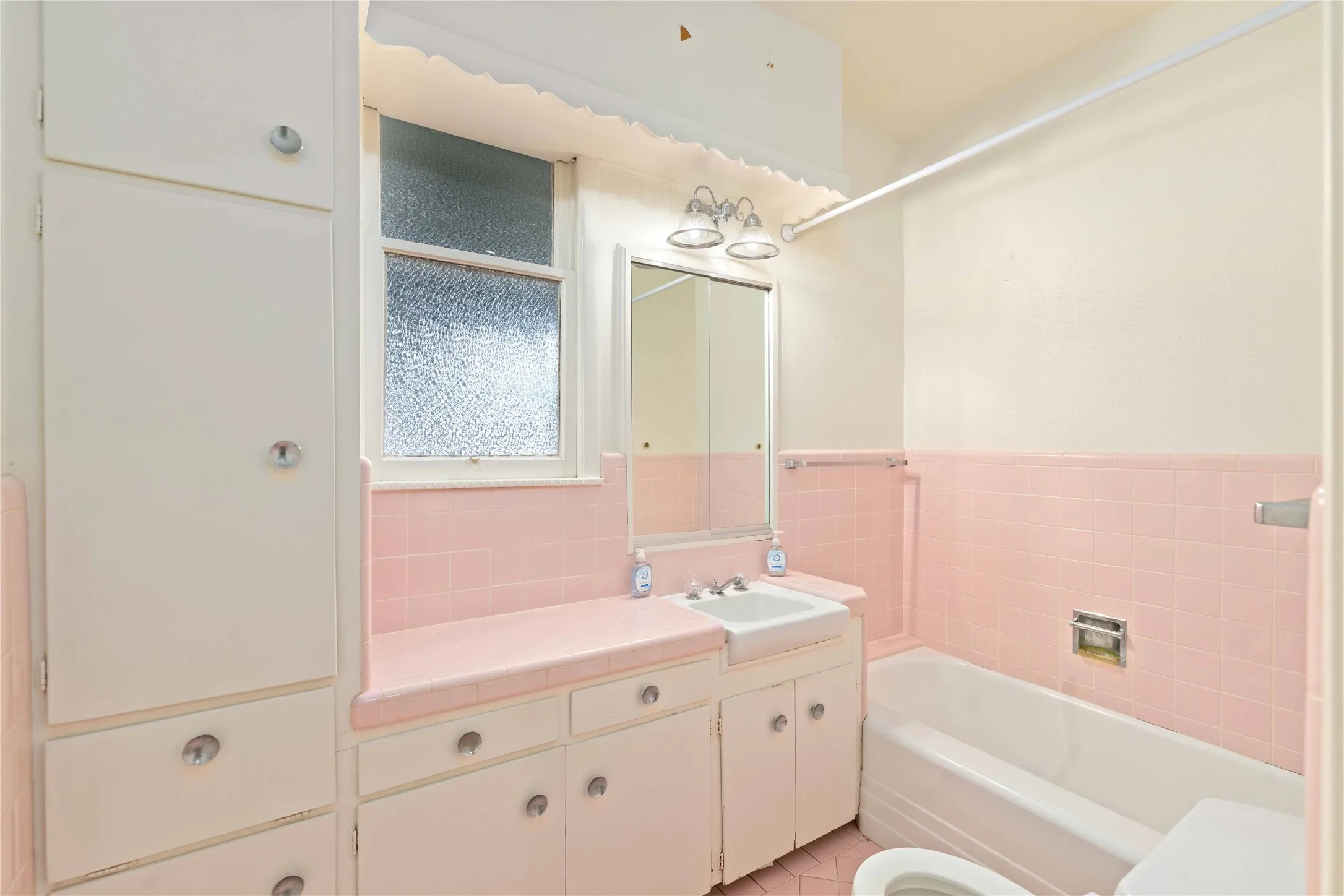 Bathroom featuring custom floor-to-ceiling built-in cabinetry, ceramic tile surround with pink tiled walls, integrated countertop with a drop-in sink, and a medicine cabinet with dual-light fixture