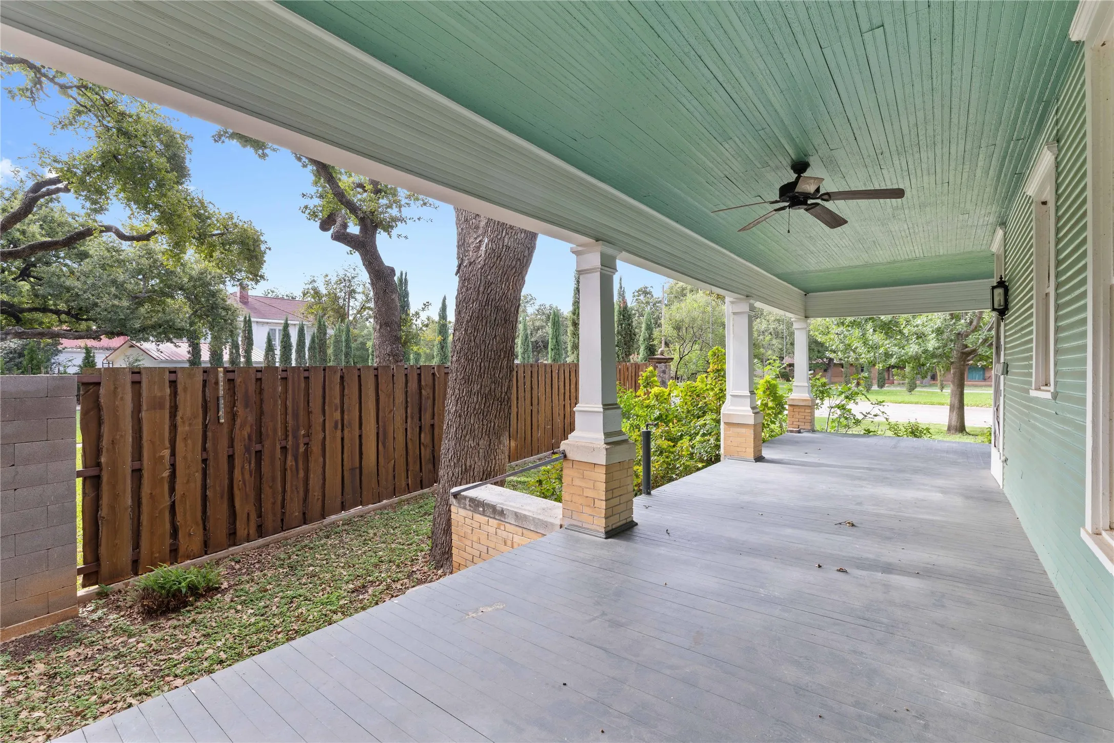 Covered porch featuring wood-finish decking, painted beadboard ceiling, ceiling fan, and masonry-supported columns