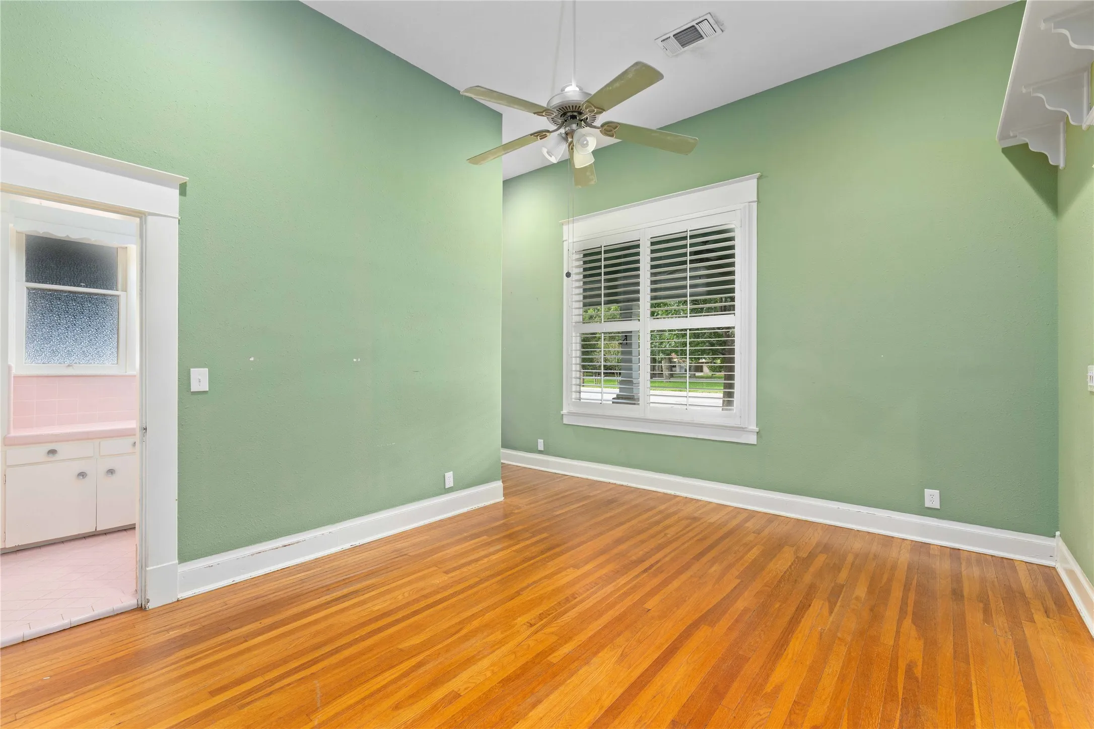 High-ceiling room featuring wood-finish flooring, multi-pane window with white shutters, and a ceiling-mounted fan with integrated light fixture