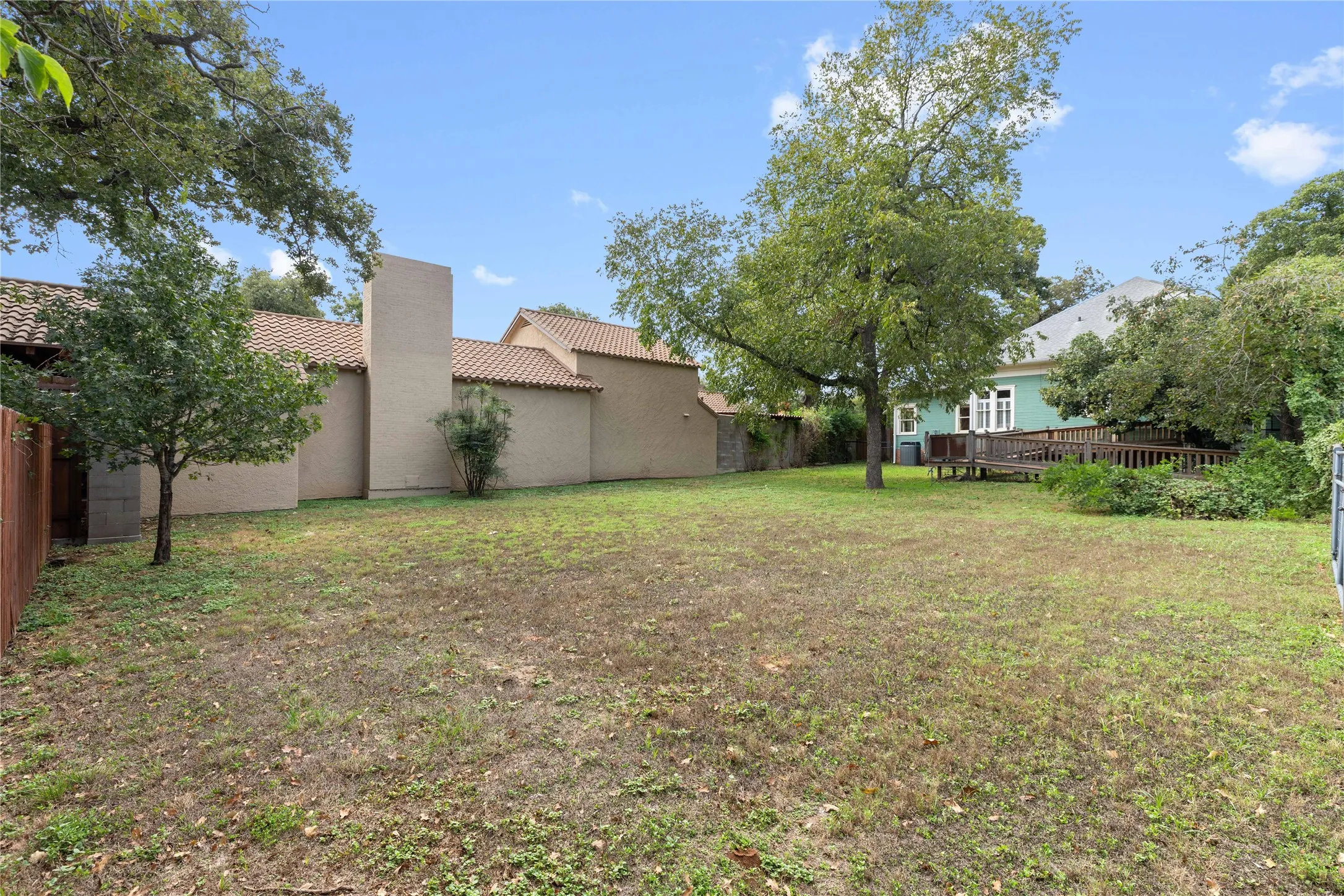 Expansive backyard featuring a leveled grass lawn, mature trees, wood decking, and masonry exterior walls