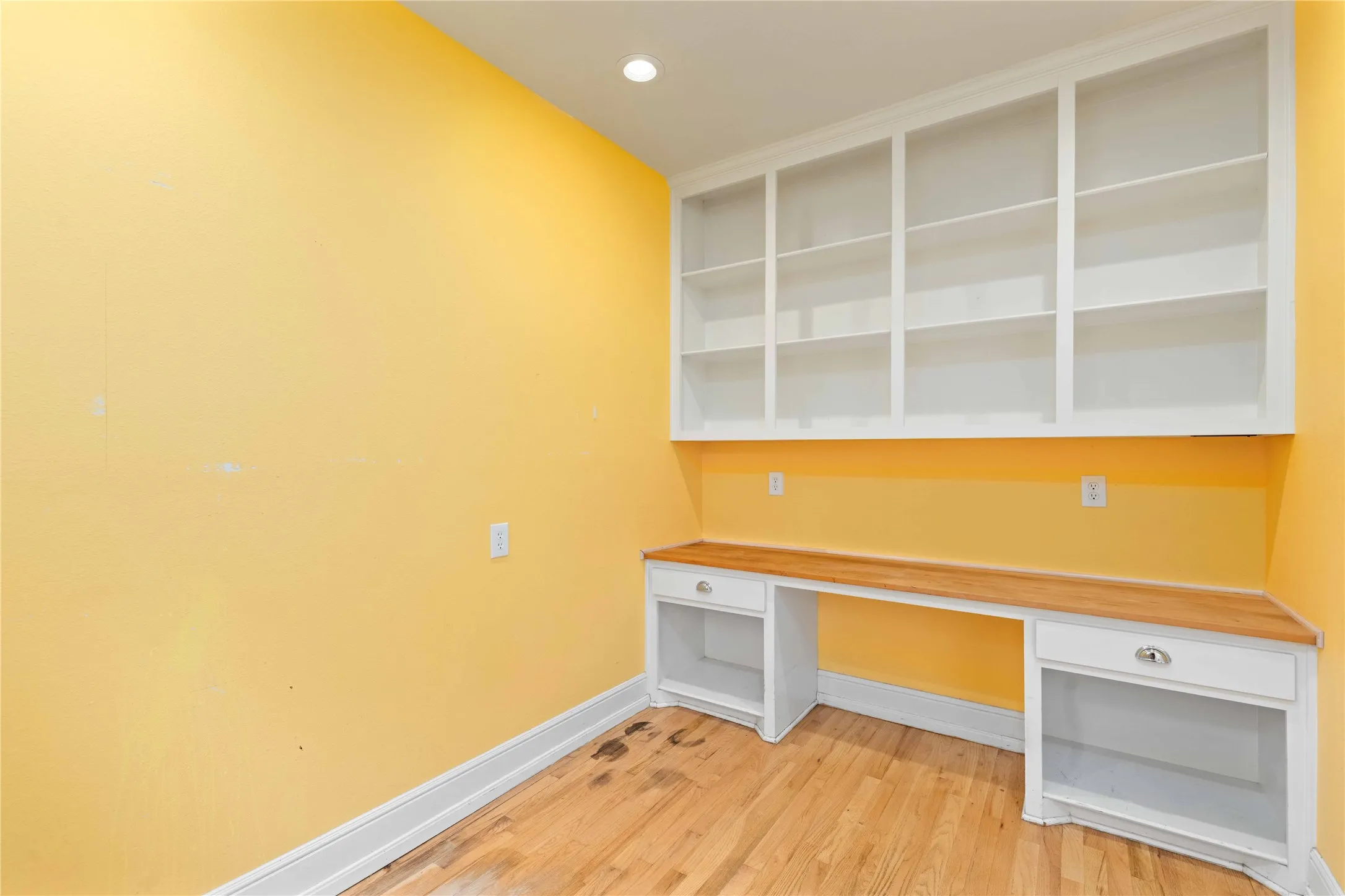 Built-in shelving, wood-surface desk with integrated drawers, and wood-finish flooring