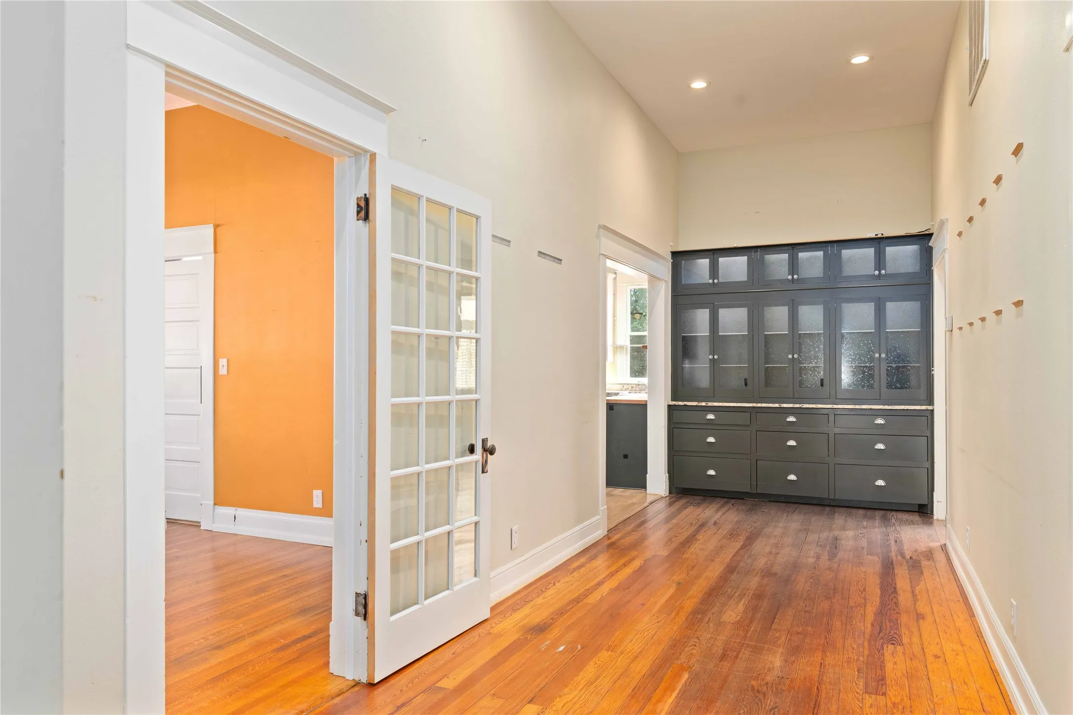 Vaulted ceilings, dark-finish built-in cabinetry with glass-paneled uppers, wood-finish flooring, and French door entry