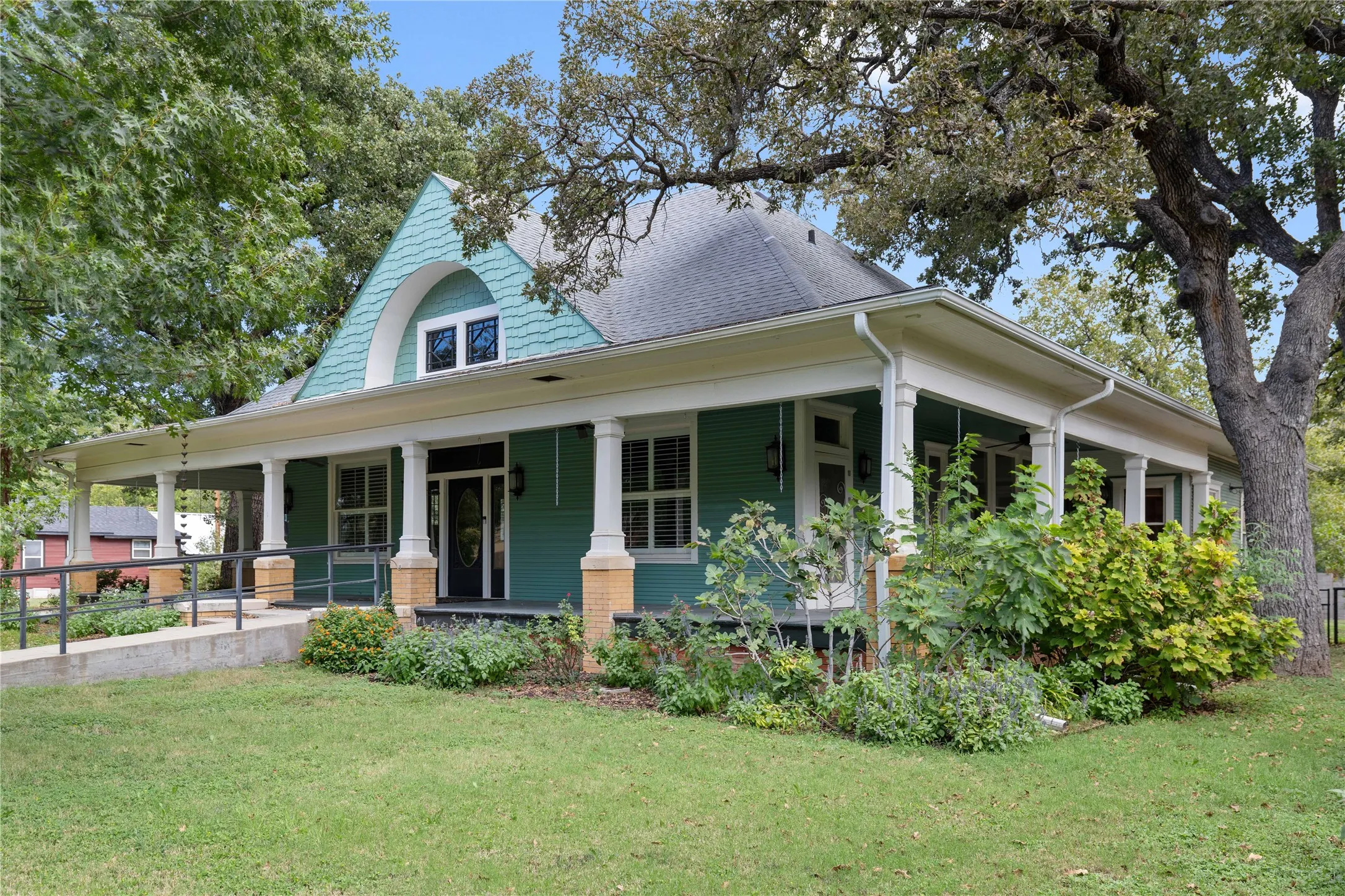 Craftsman-style residence featuring a wraparound porch, prominent arched gable detailing, shake-shingle siding, brick-base columns, and an exterior accessibility ramp