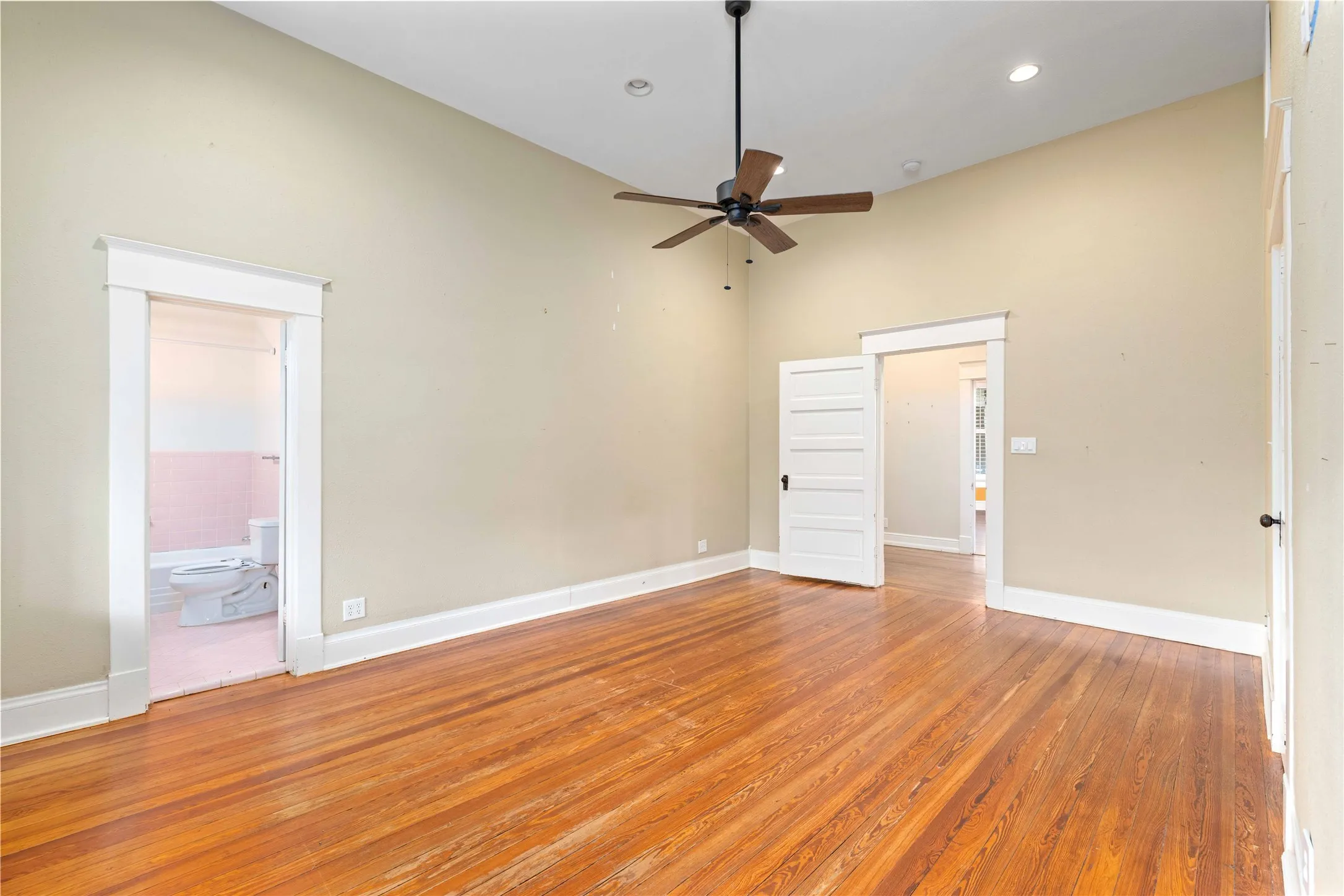 Vaulted ceilings featuring recessed lighting and a central ceiling fan, wood-finish flooring, and classic interior doors with white trim