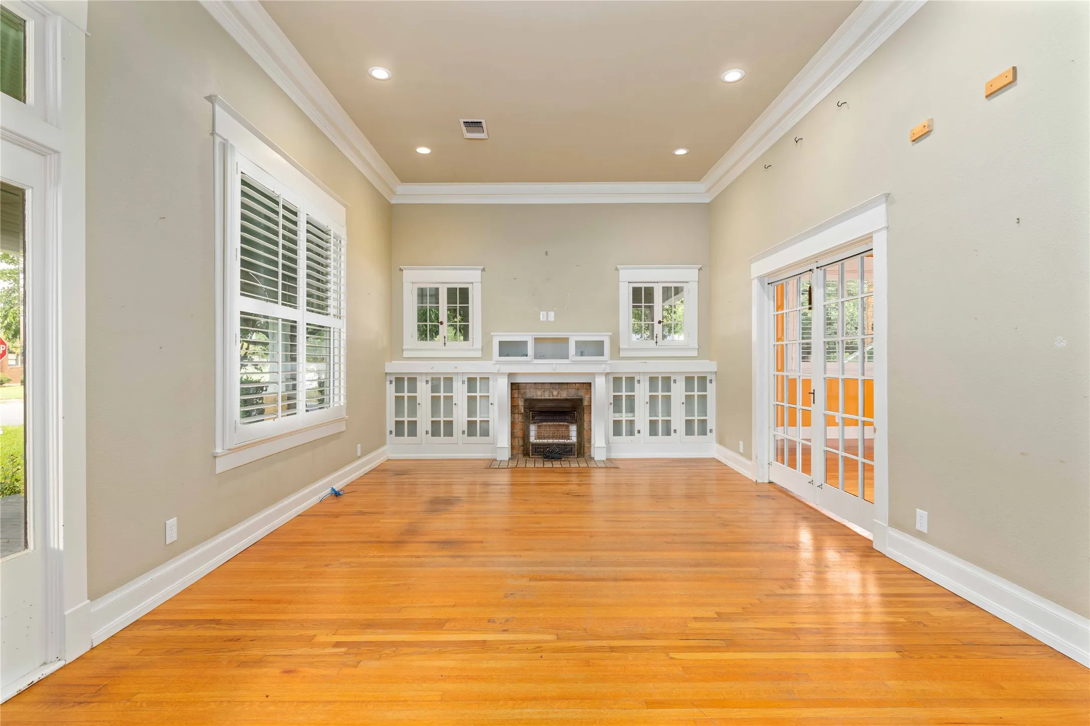 Living area featuring wood-finish flooring, tray ceiling with recessed lighting, crown molding, built-in cabinetry, and a masonry fireplace