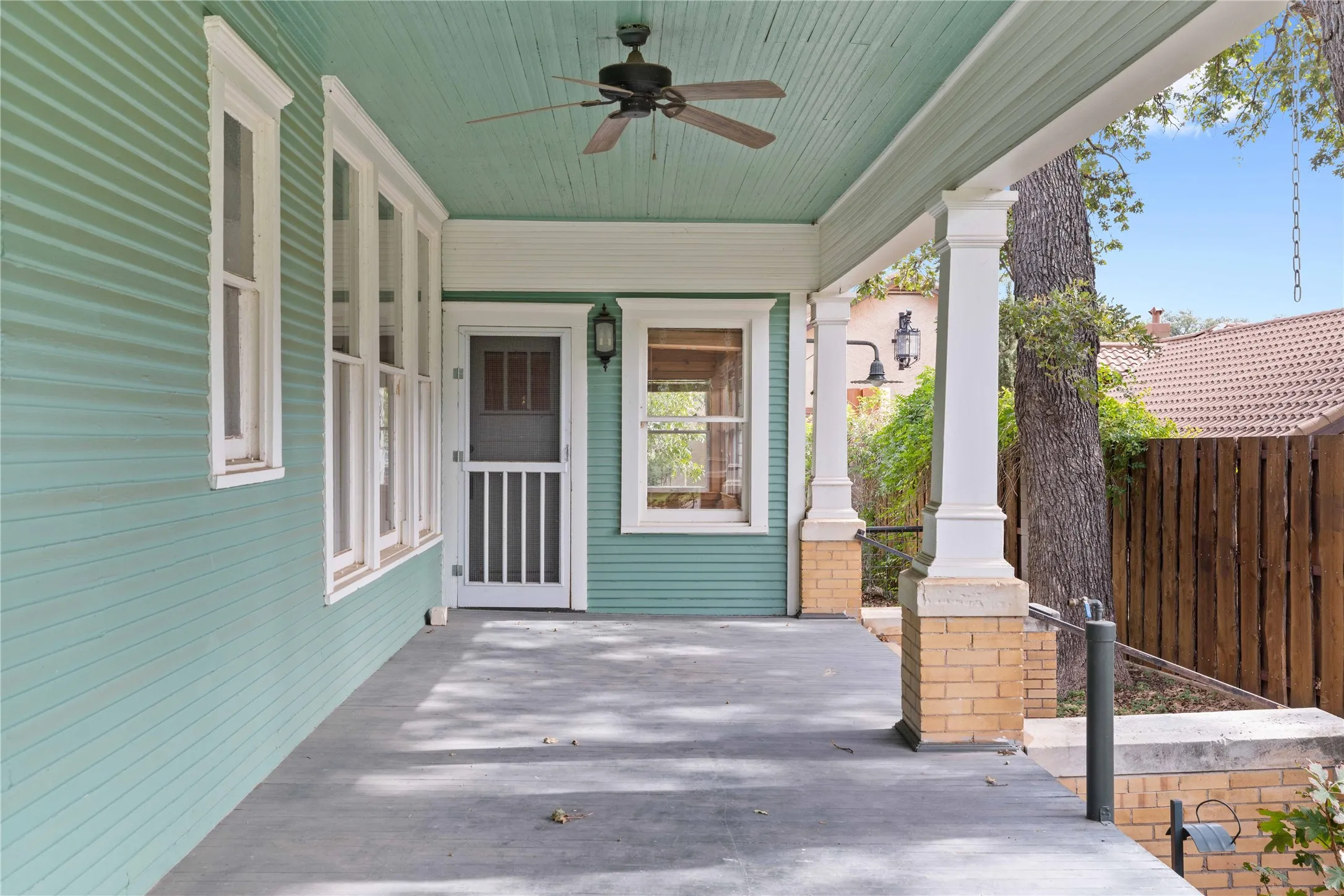Covered porch featuring lap siding, paneled wood columns with masonry bases, a ceiling-mounted fan, and a wood-frame screen door
