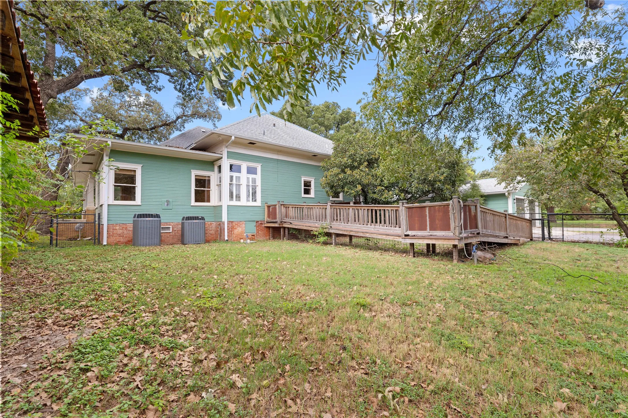 Exterior featuring lap siding, brick foundation, elevated wood deck with railing, and mature trees on the grounds