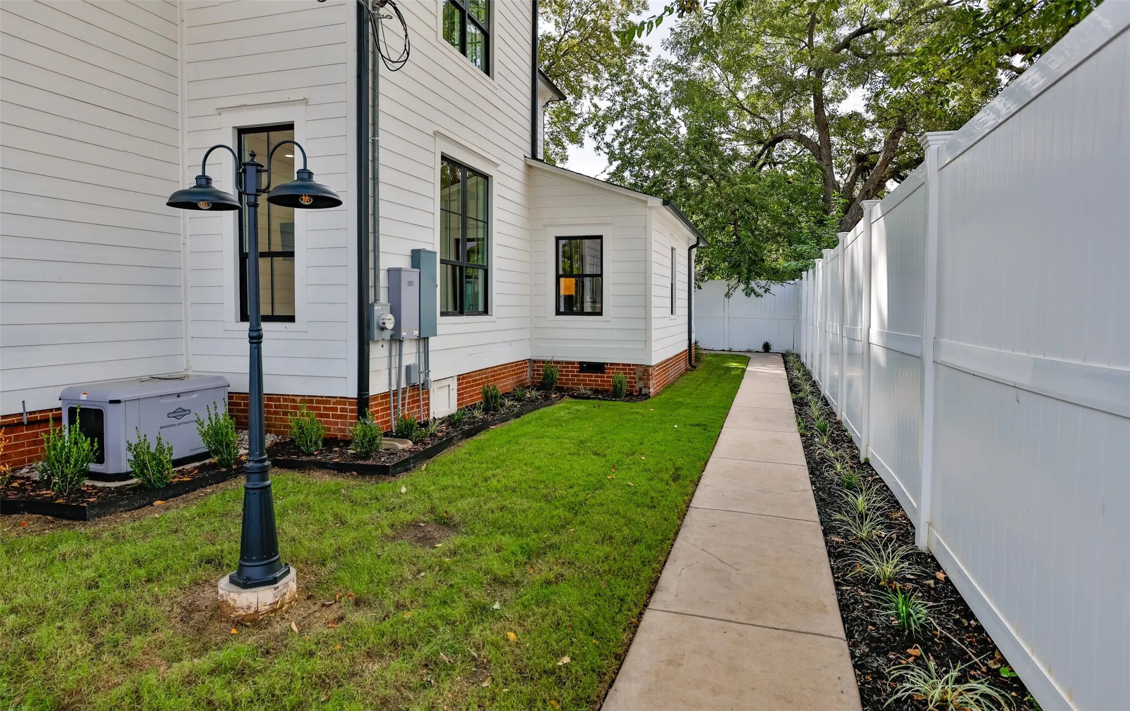 Exterior side yard featuring white siding, a red brick foundation, walkway, full-height vinyl privacy fencing, and a metal lamppost