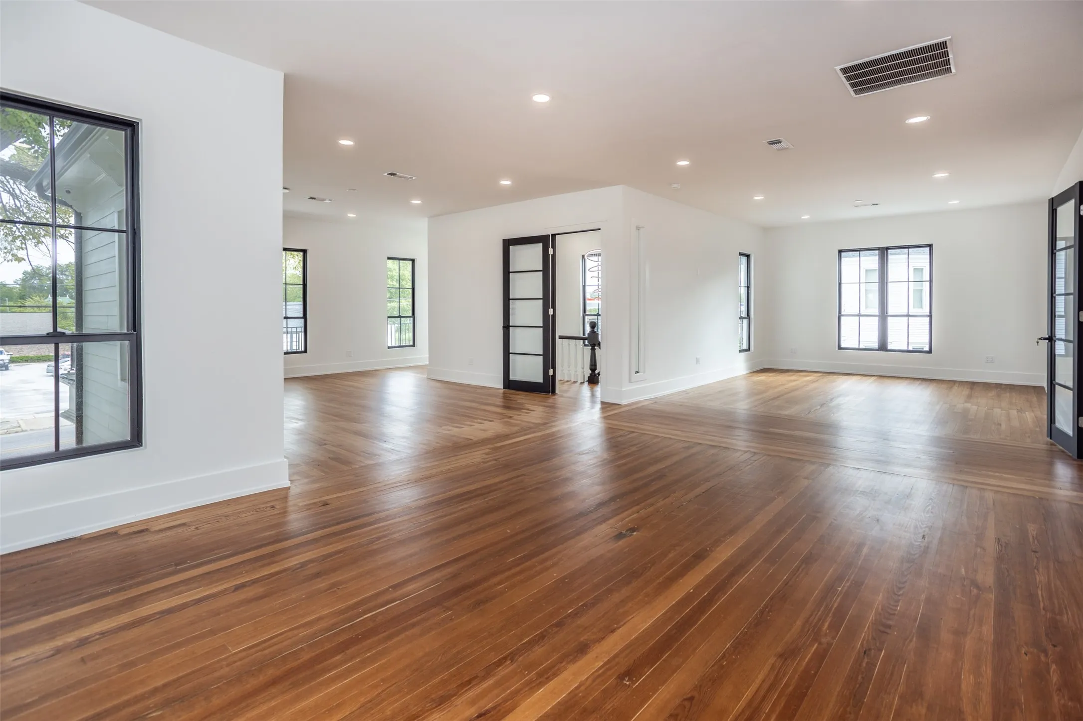 Open-concept interior featuring wood-finish flooring, recessed lighting, multi-pane windows, and interior doors with glass paneling