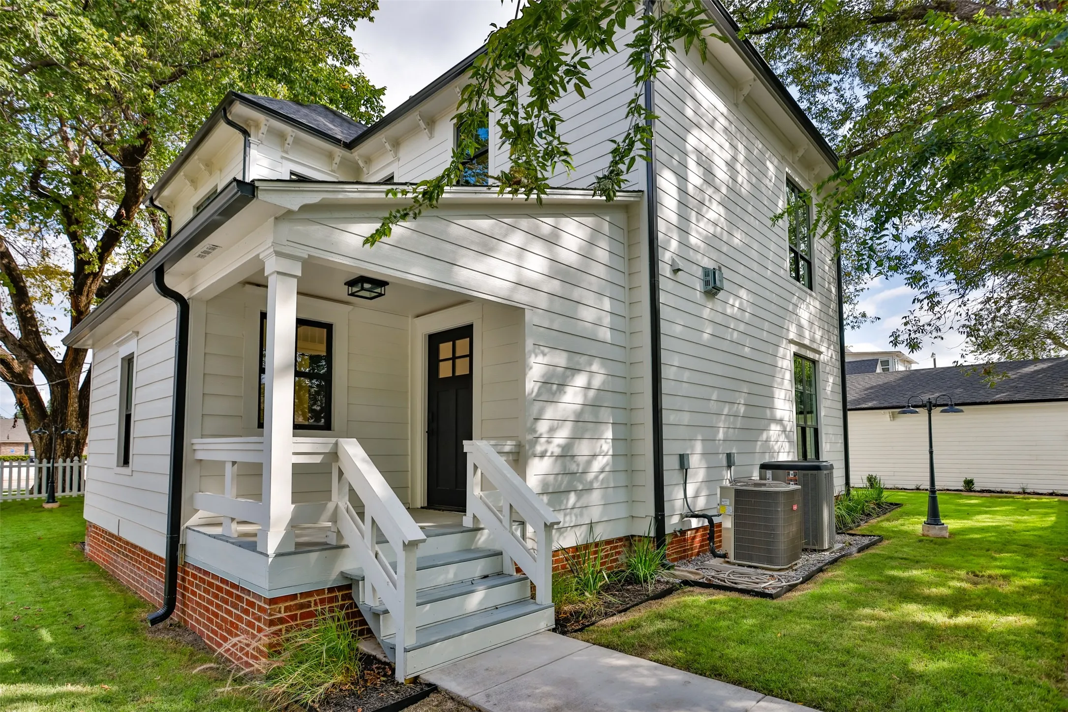 Two-story exterior featuring white siding, a red brick foundation, a covered porch with staircase, and framed multi-pane windows