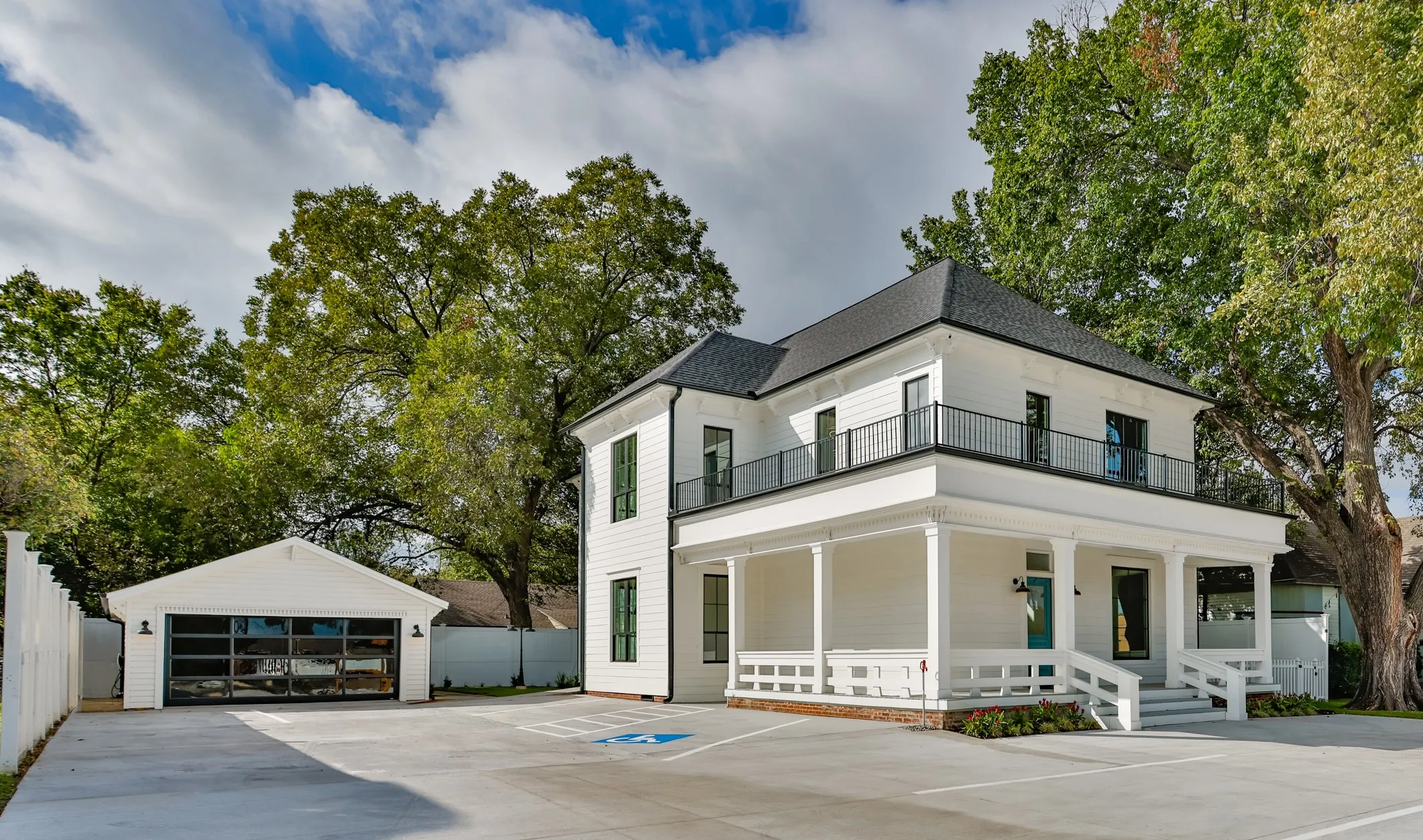 Two-story exterior featuring white siding, a covered front porch with decorative railings, a second-story balcony with metal railings