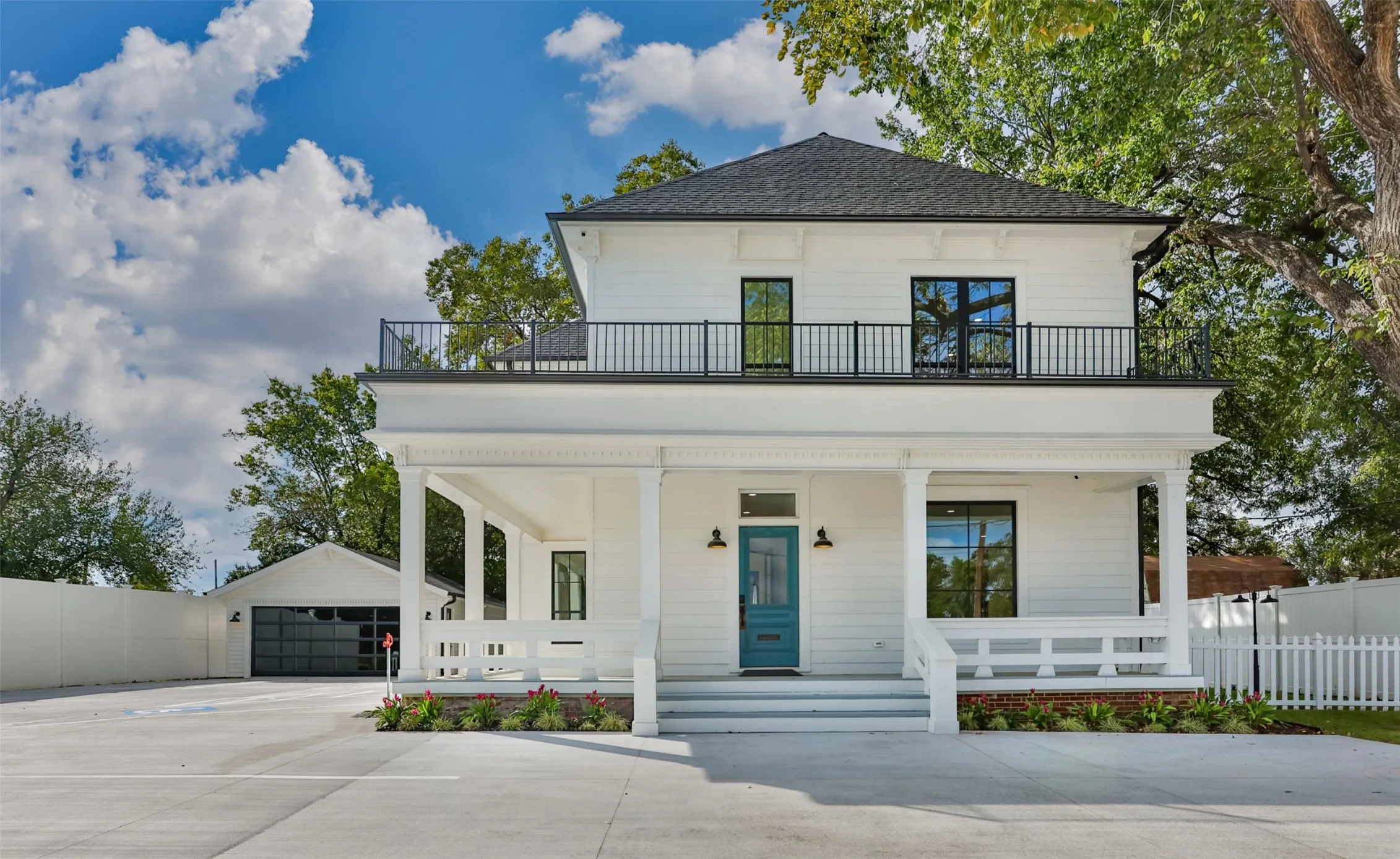 Two-story exterior featuring white siding, a covered front porch with decorative millwork, a second-story balcony with black metal railing