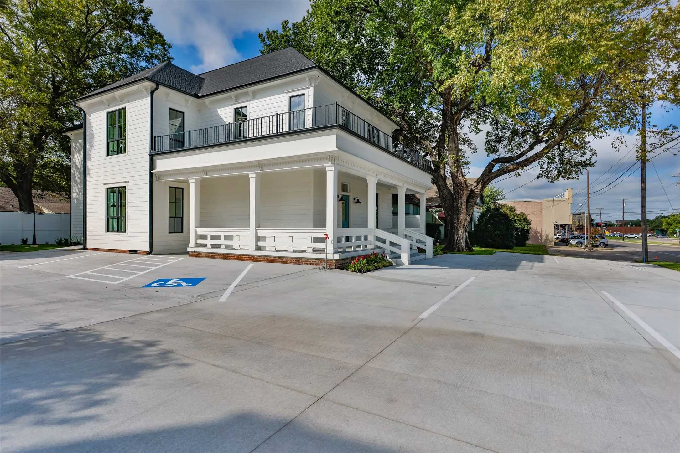 Two-story exterior featuring white siding, a wraparound covered porch, second-story balcony with metal railing, and parking area