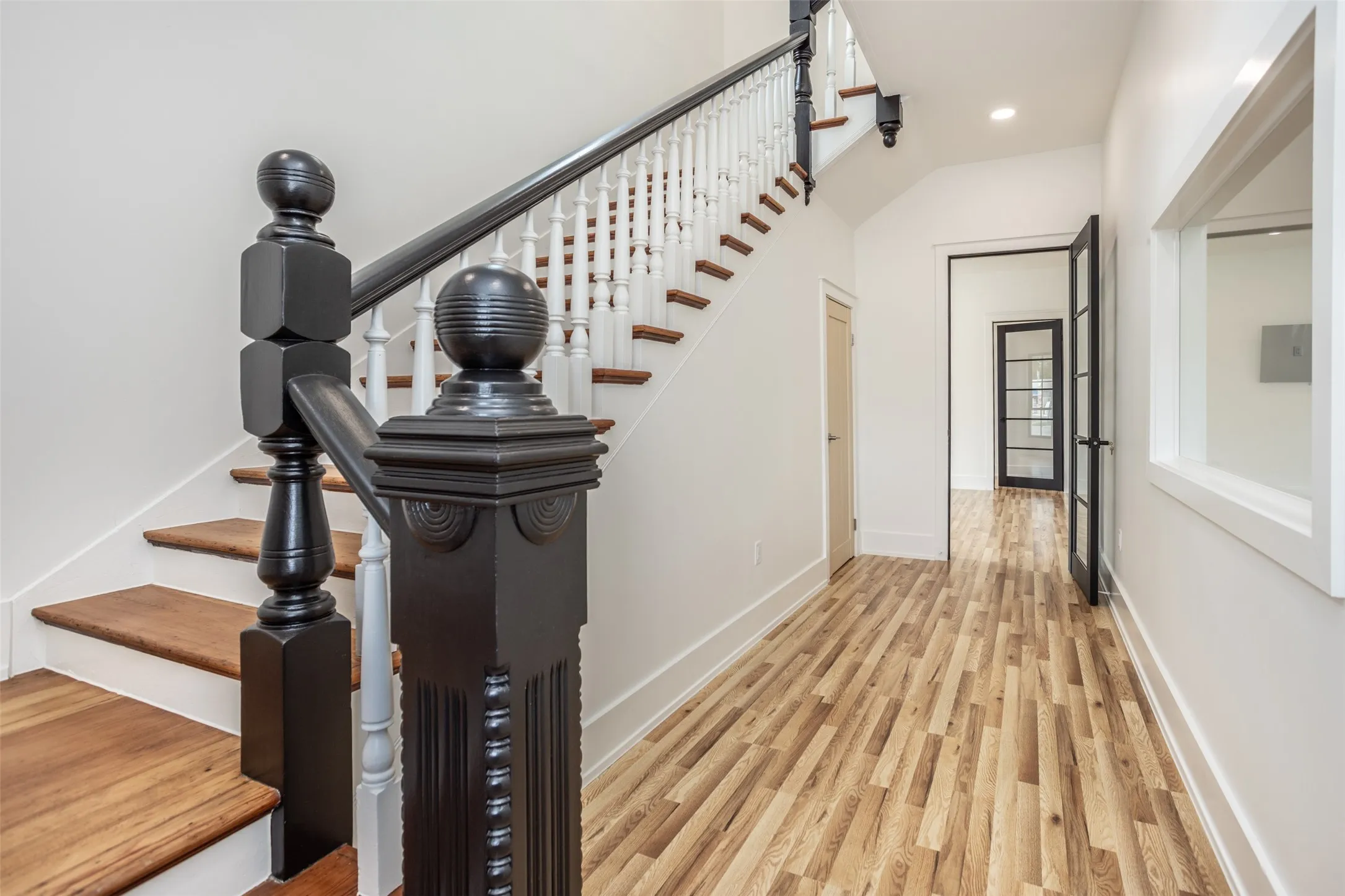 Staircase featuring wood-finish treads, a contrasting black and white balustrade with an ornate newel post, and wood-finish flooring