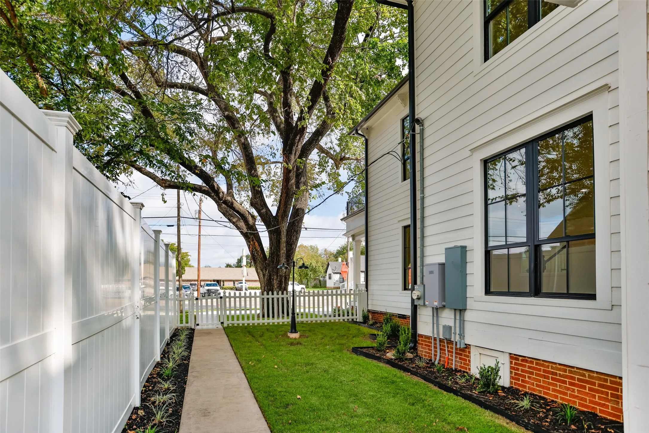 Exterior side yard featuring white siding, a brick foundation, full-height white vinyl privacy fencing, a manicured lawn, and a white picket fence
