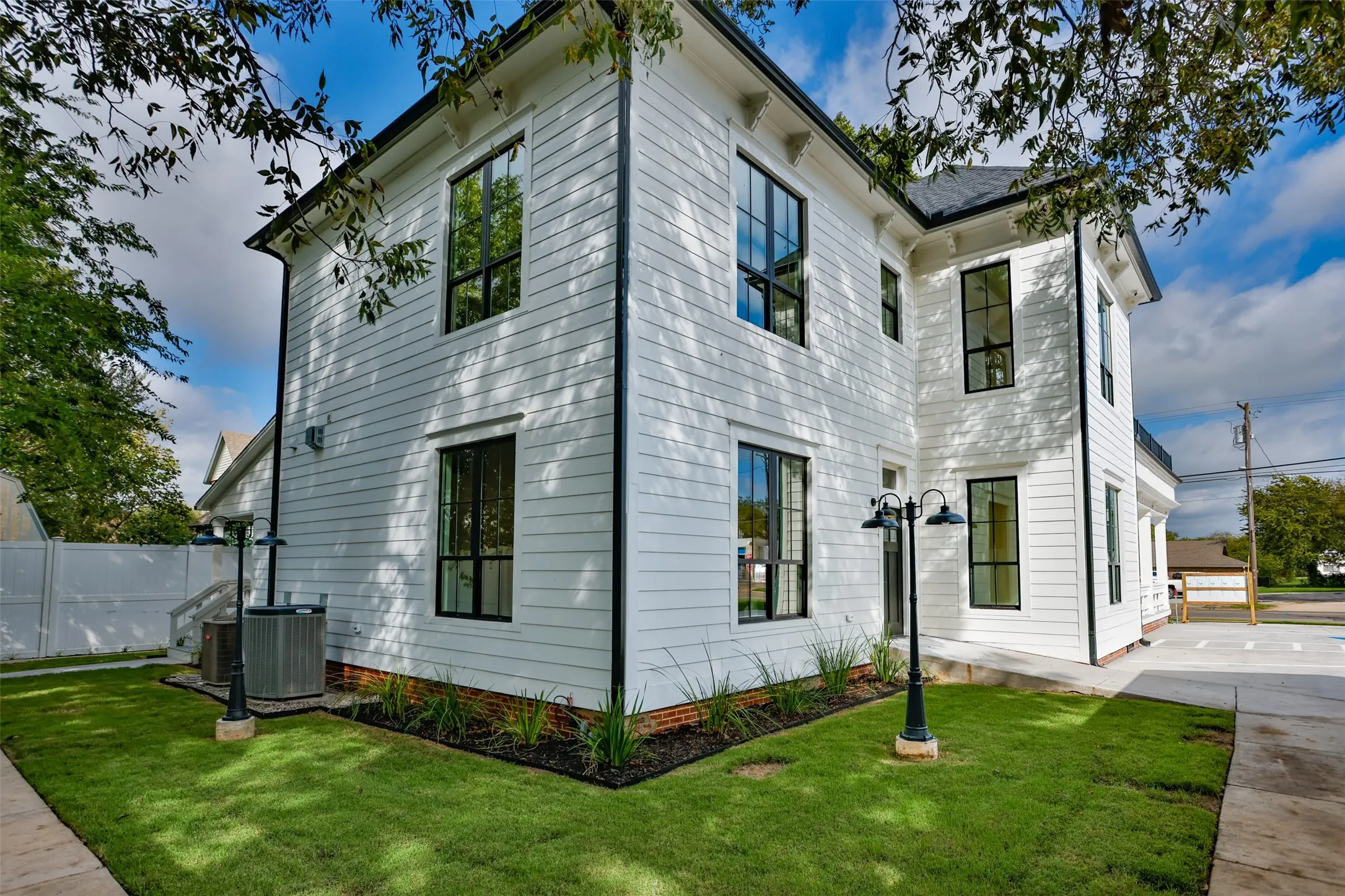 Two-story exterior featuring white siding, windows, a brick foundation, and dual-headed metal post lighting
