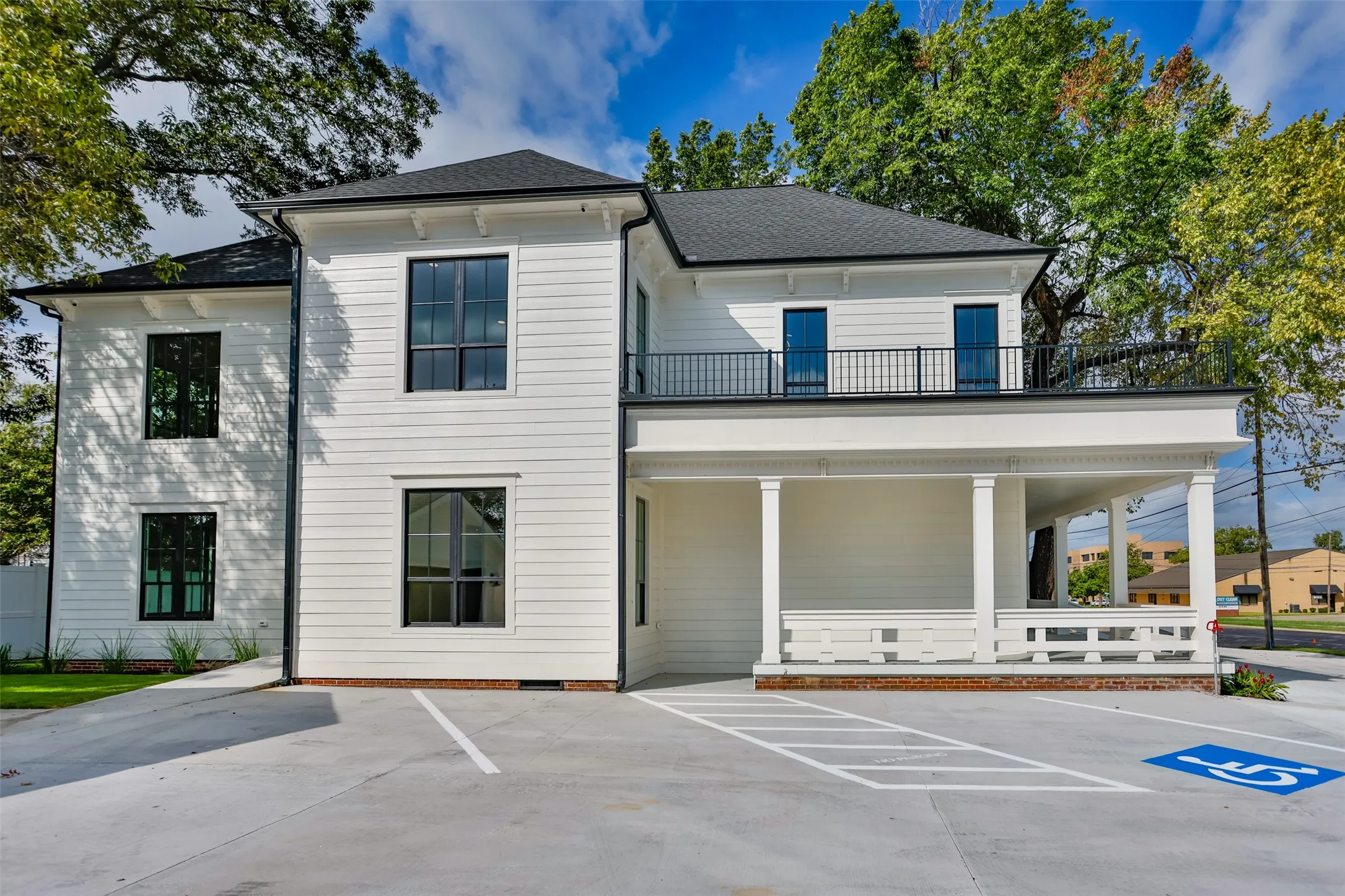Two-story exterior featuring white siding, a covered porch with decorative corbels, new roof, a railed upper-level balcony, and framed multi-pane windows