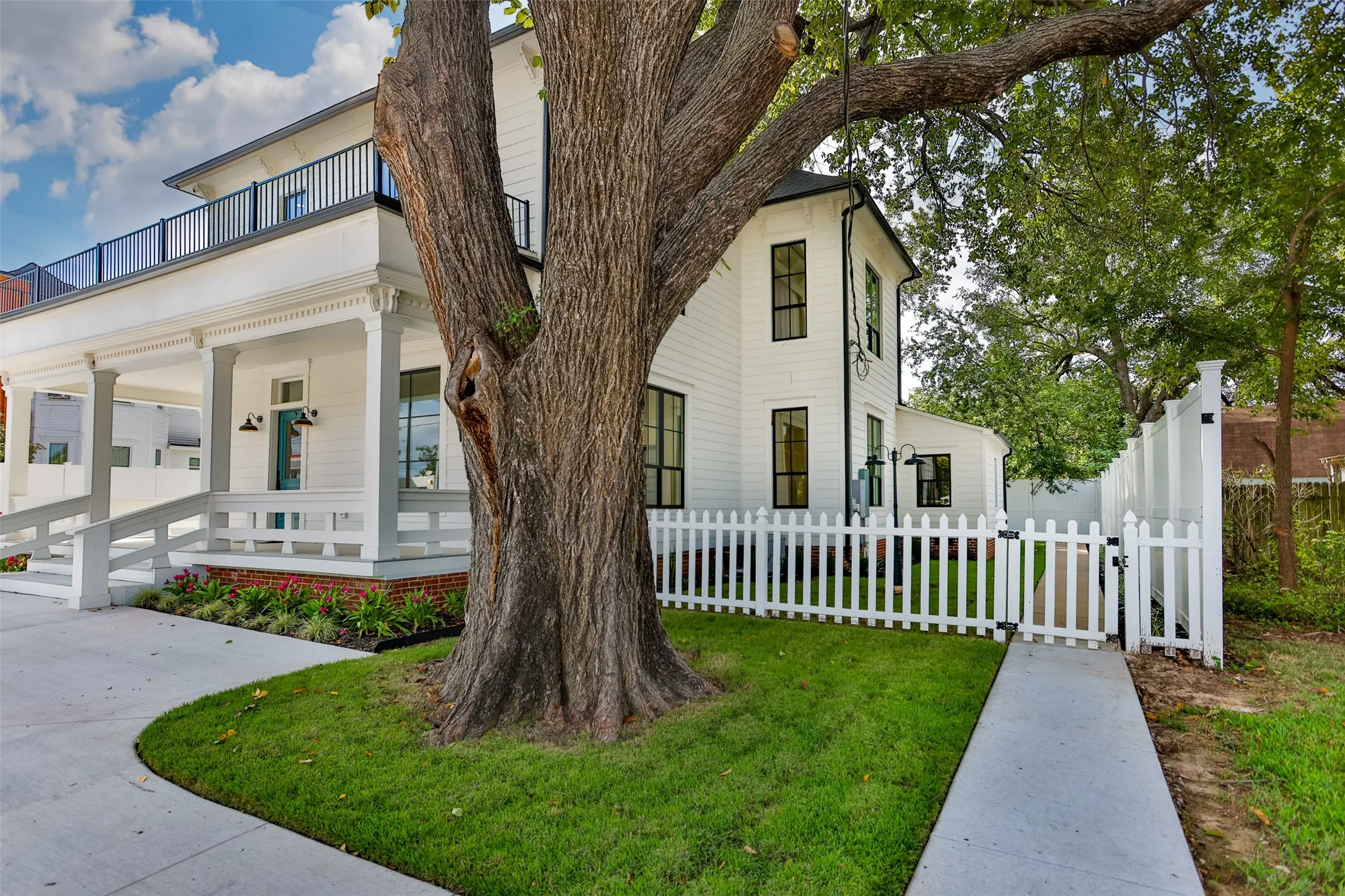 Two-story exterior featuring white siding, a covered front porch, second-level balcony with black railing, and white picket fencing