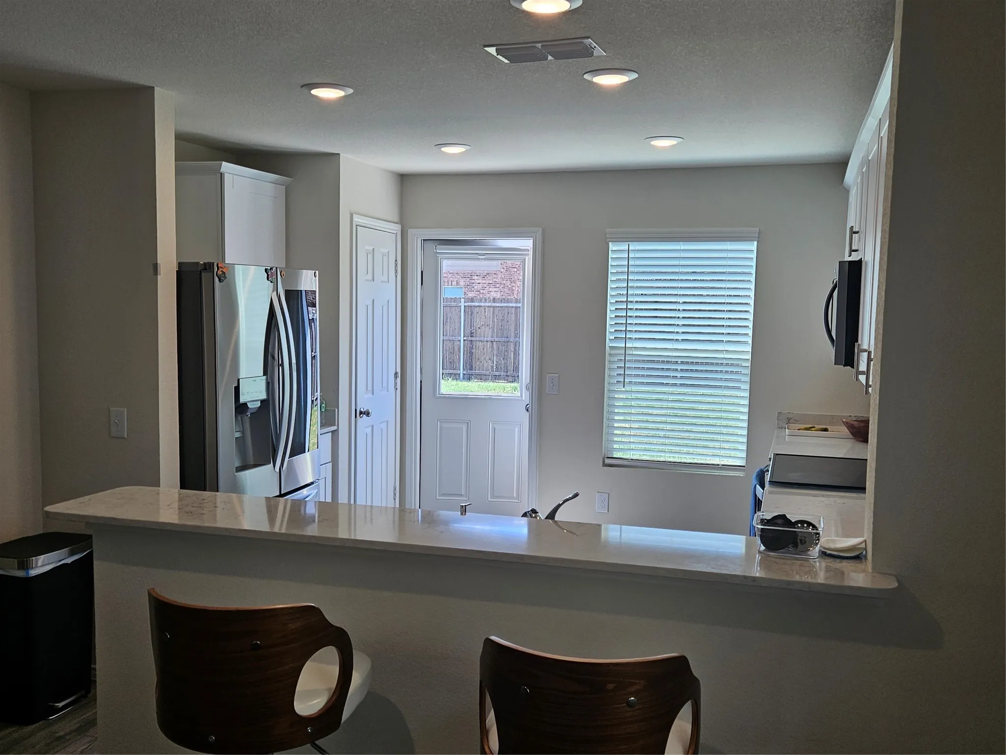 Kitchen featuring a breakfast bar with stone-surfaced countertop, stainless steel refrigerator, recessed lighting, and white cabinetry