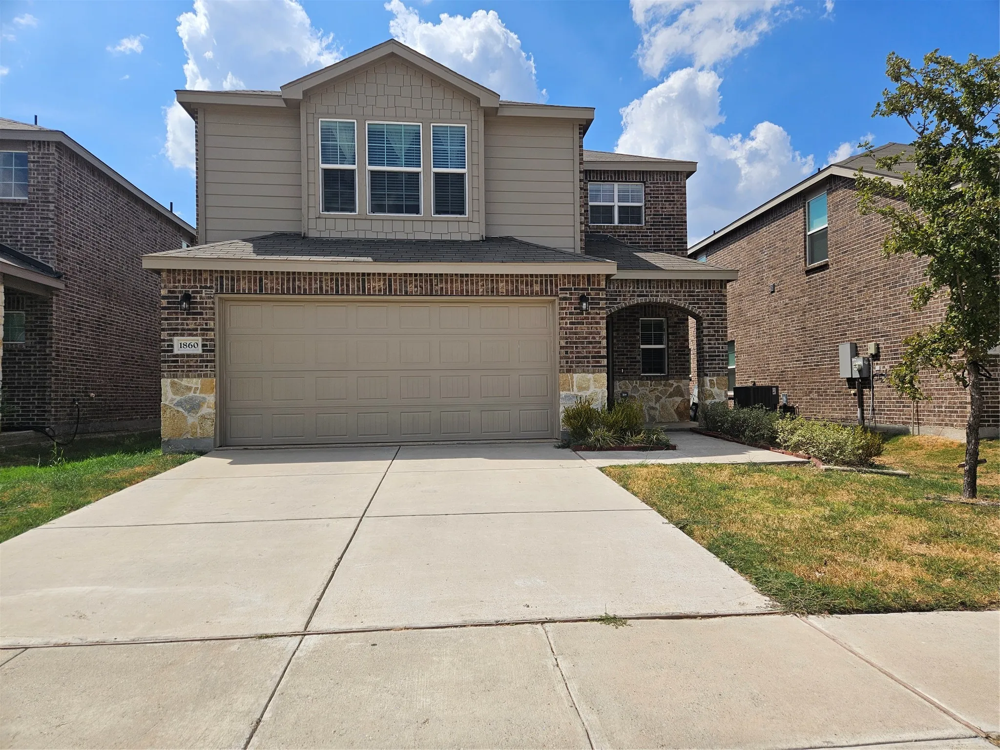 Two-story exterior featuring a brick and stone facade, horizontal siding, a multi-paneled garage door, and a covered entryway
