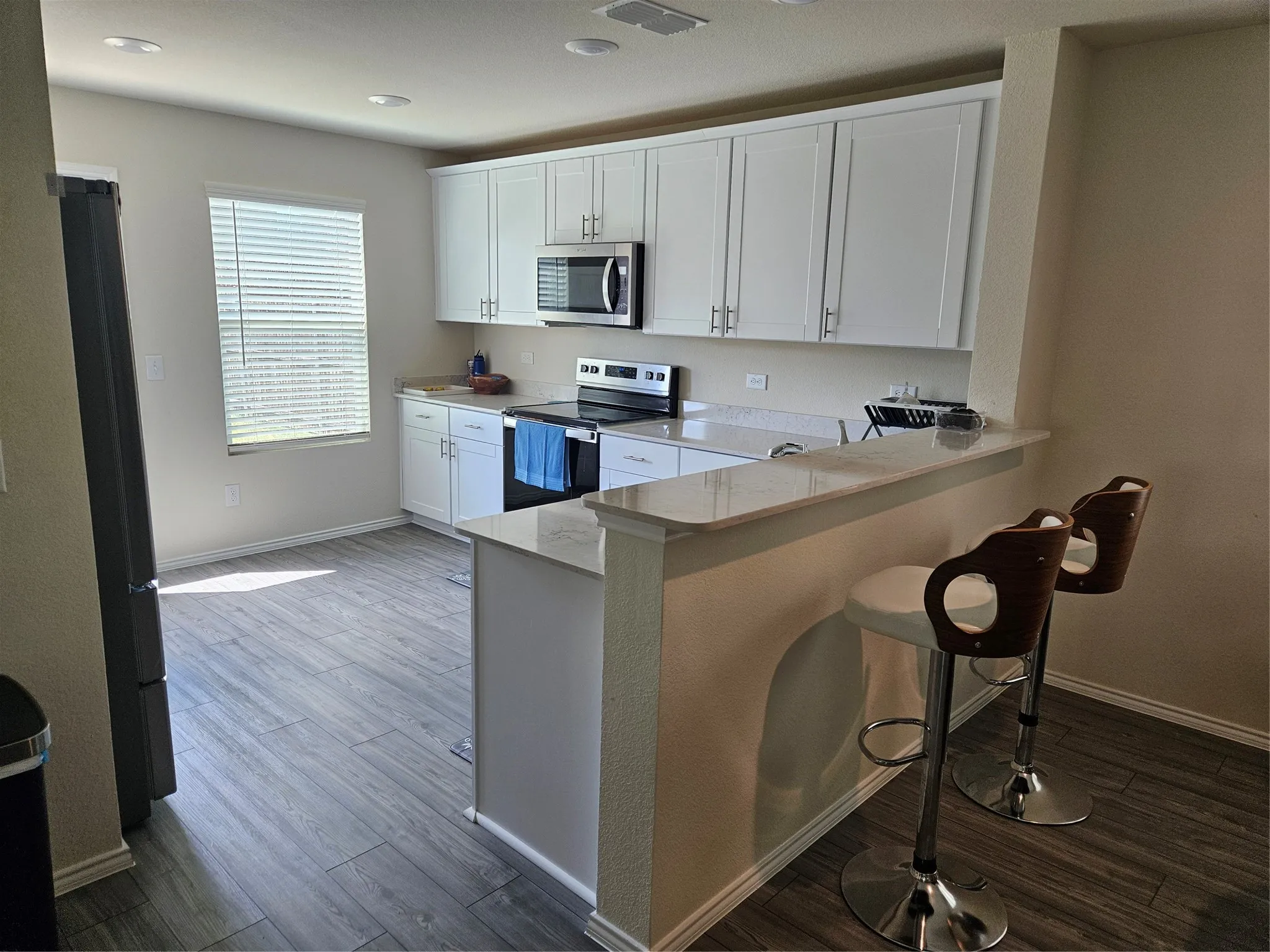 Kitchen featuring white cabinetry, solid-surface countertops, wood-finish flooring, stainless steel appliances, and a peninsula breakfast bar