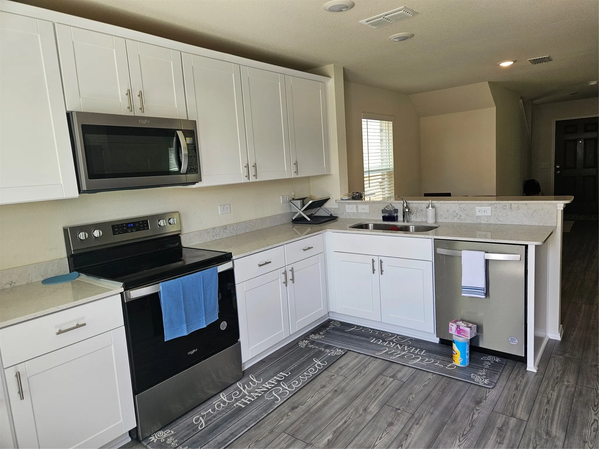 Kitchen featuring white Shaker-style cabinetry, stainless steel appliances, neutral stone-finish countertops, and wood-finish flooring