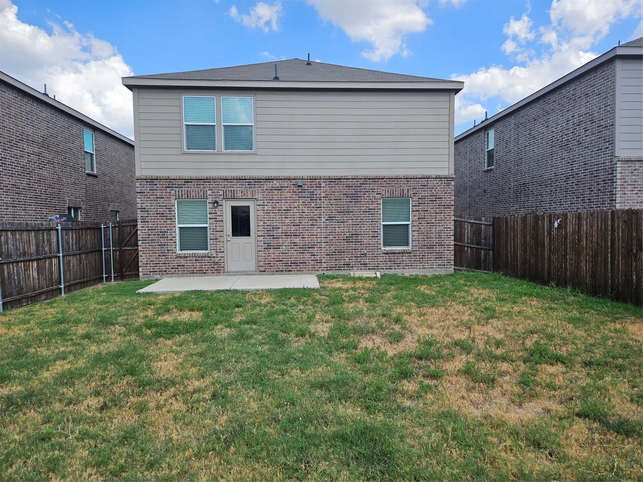 Rear exterior featuring a brick and siding facade, concrete patio, and fenced-in backyard