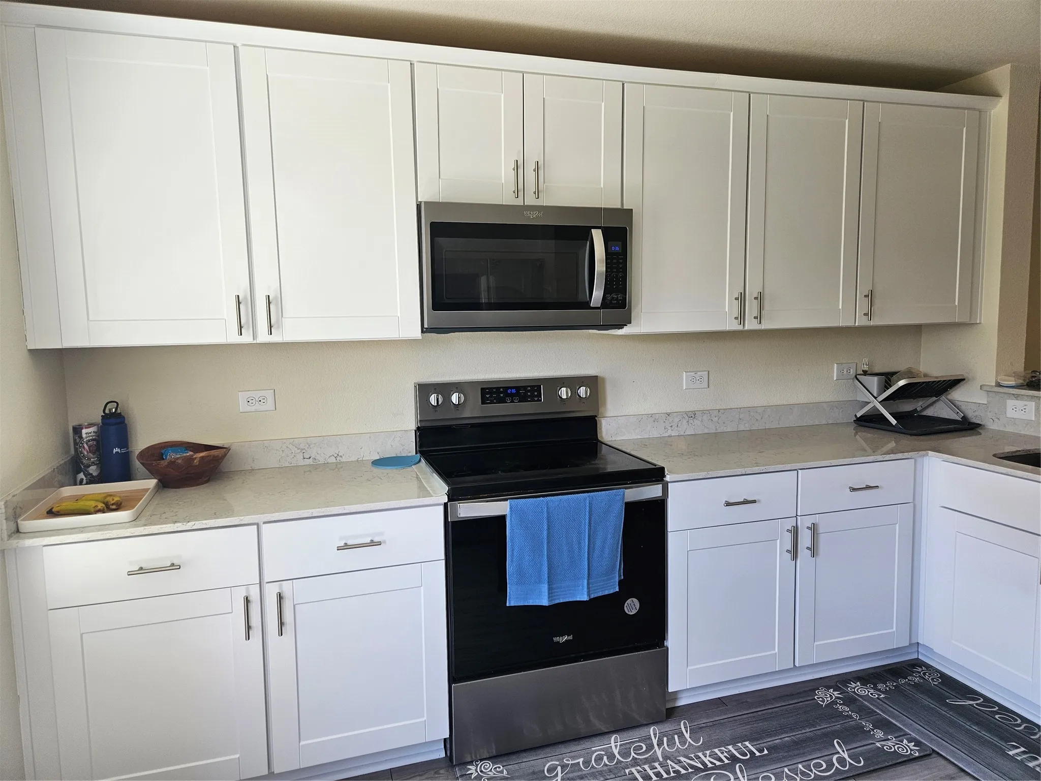 White shaker-style cabinetry, stainless steel appliances, neutral stone-finish countertops, and wood-finish flooring