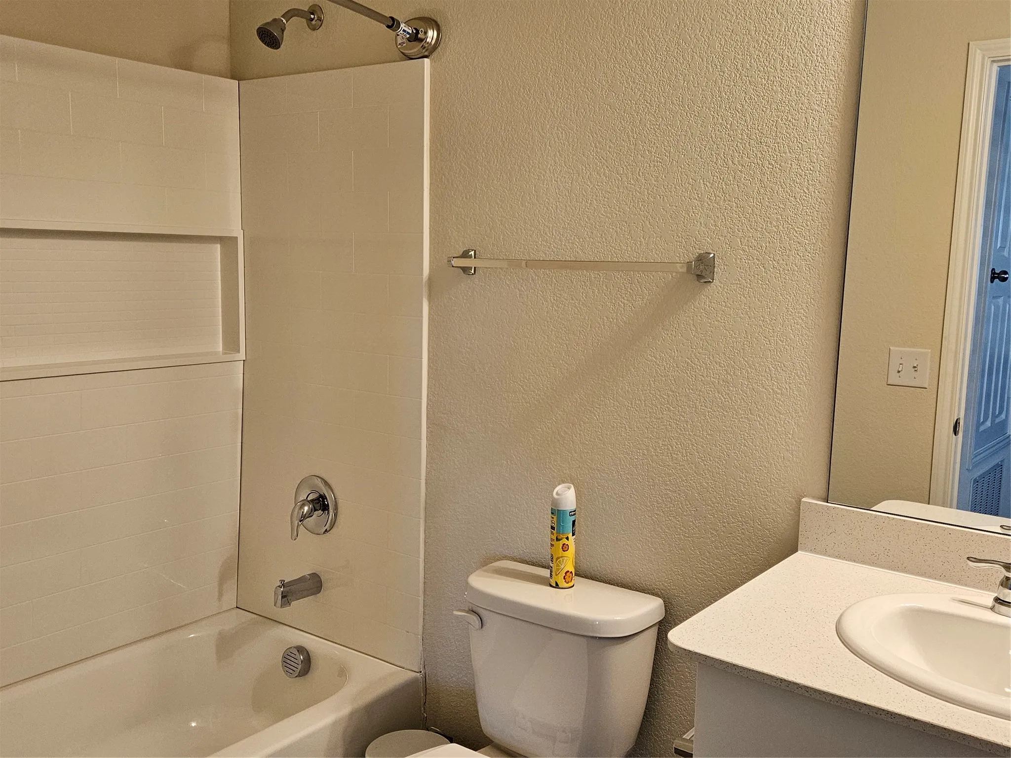 Bathroom featuring a shower and tub combination with built-in shelving, chrome fixtures, a wall-mounted towel bar, and a vanity with an integrated basin