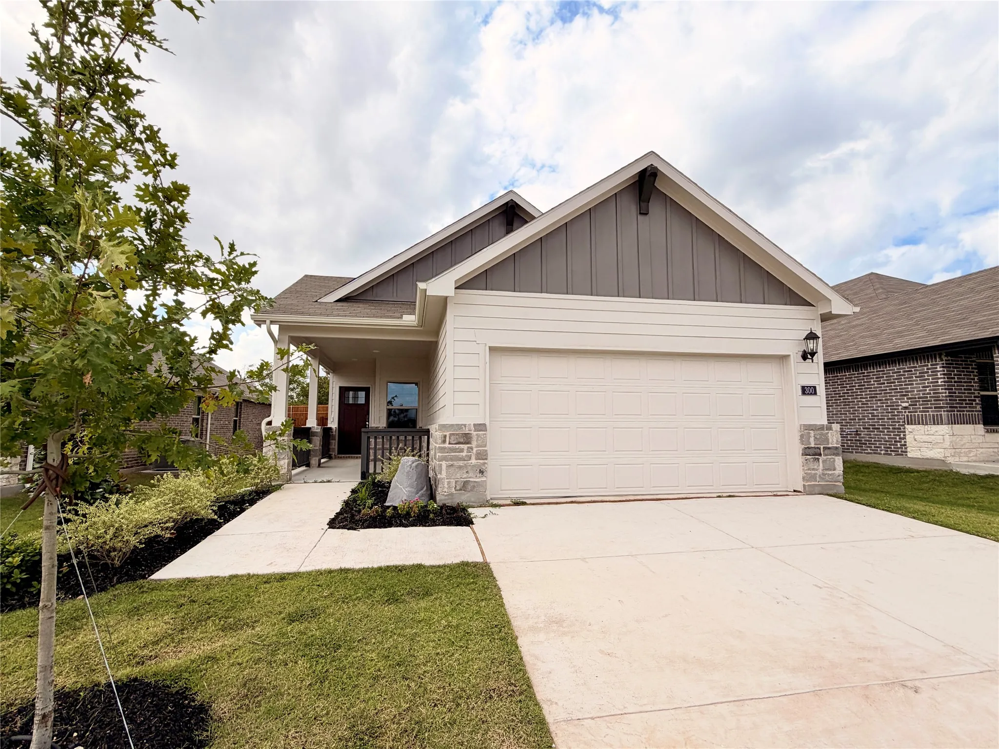 Single-story exterior featuring a mix of horizontal siding and vertical board-and-batten siding, stone masonry accents, a front-facing attached garage, and a covered entryway