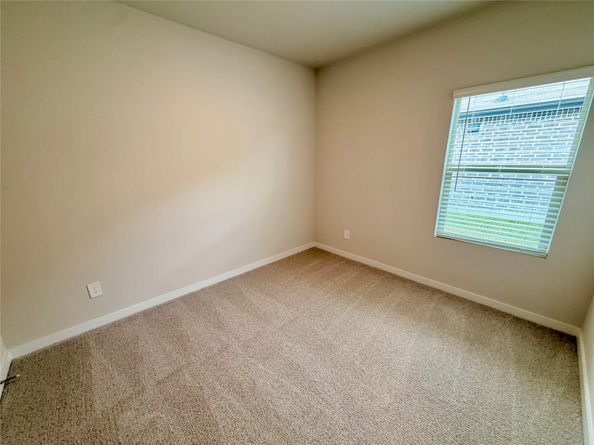 Neutral-toned interior room featuring wall-to-wall carpeting and a single-hung window with horizontal blinds